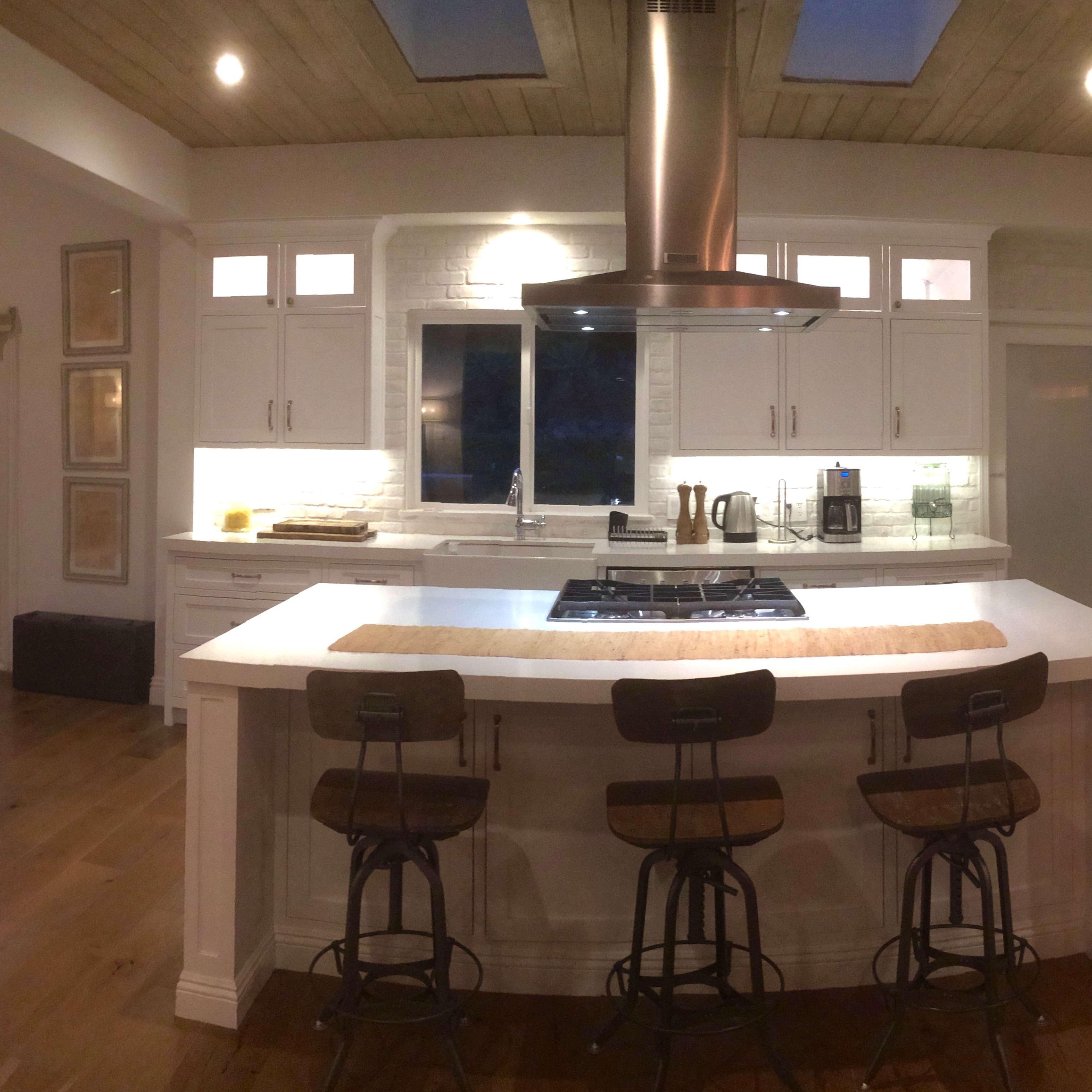 A modern kitchen featuring a central island with four bar stools, stainless steel appliances, and white cabinetry.