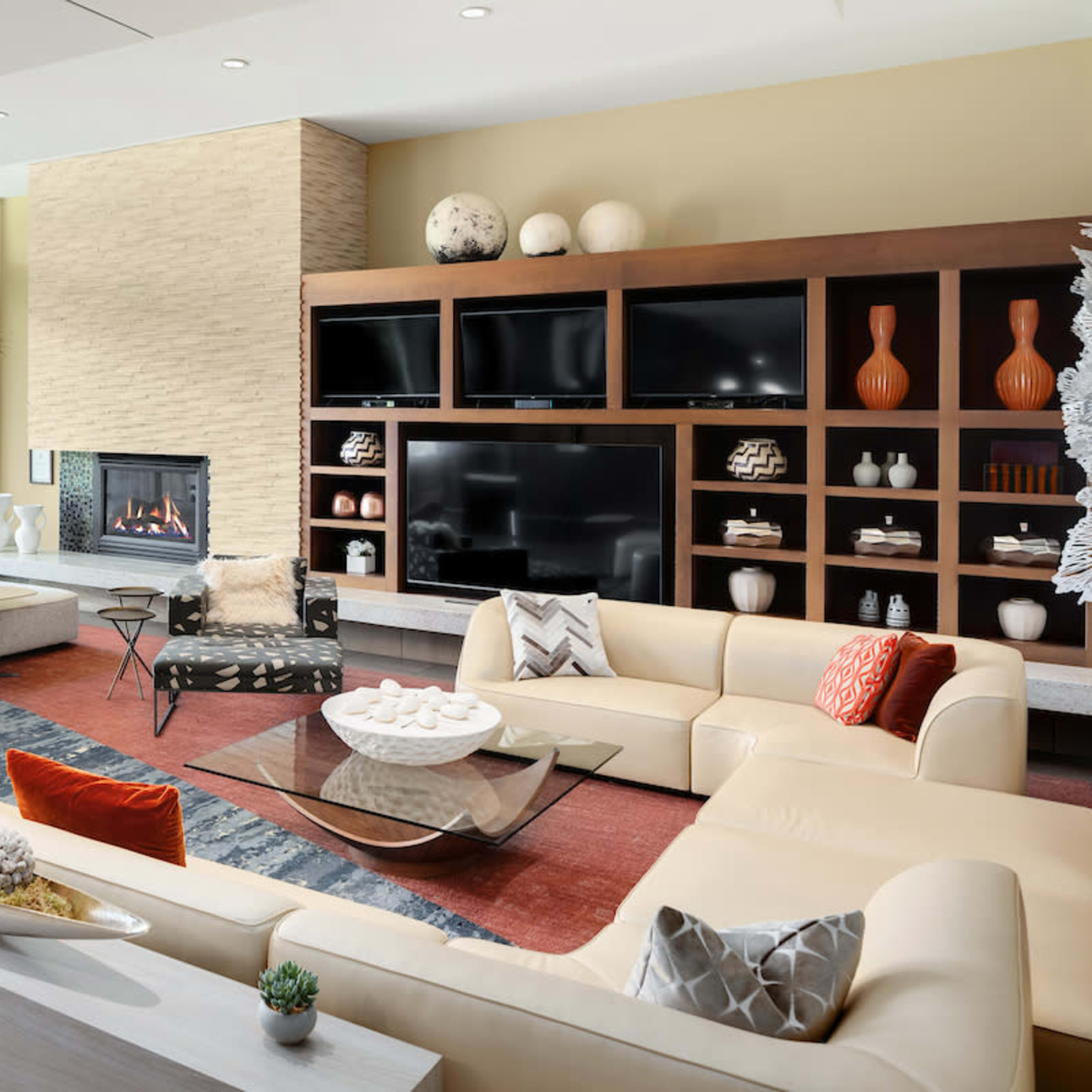 The living room features a large sectional sofa, a circular coffee table, and a fireplace, with a wall of built-in shelves displaying decorative vases.