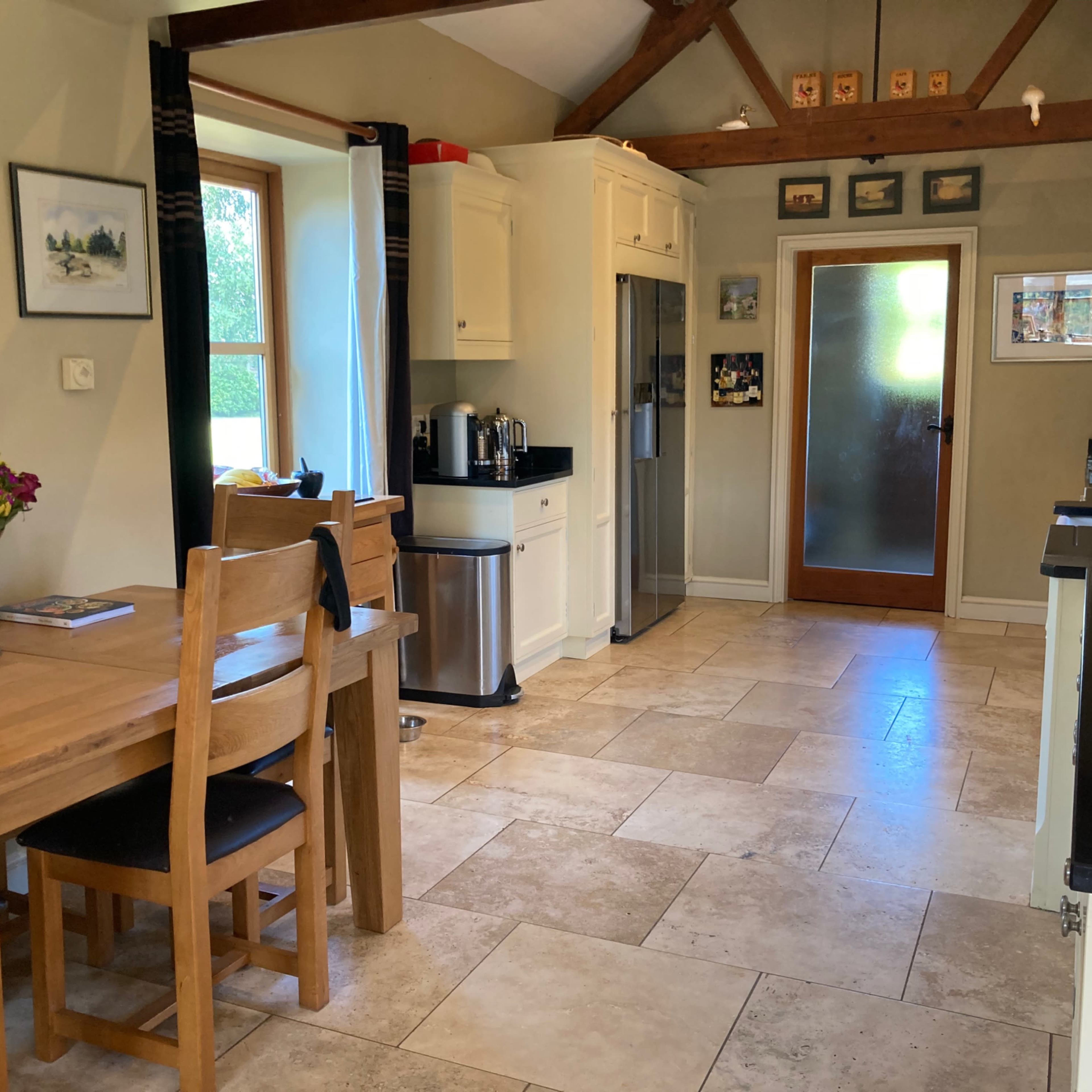 A spacious kitchen with a dining table, black countertops, a refrigerator, and a glass door leading to the outside.