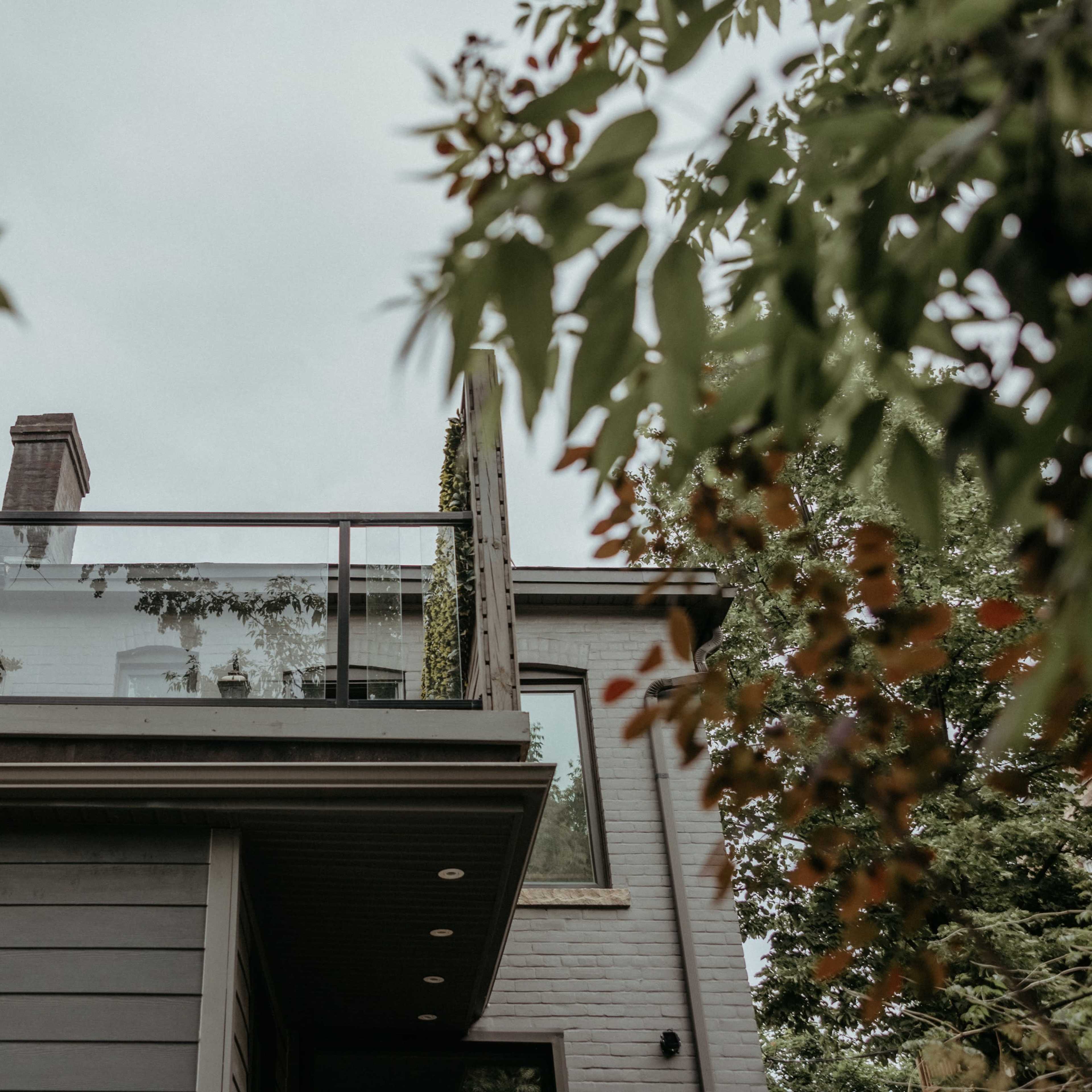 A modern house with a glass-railed balcony surrounded by greenery.