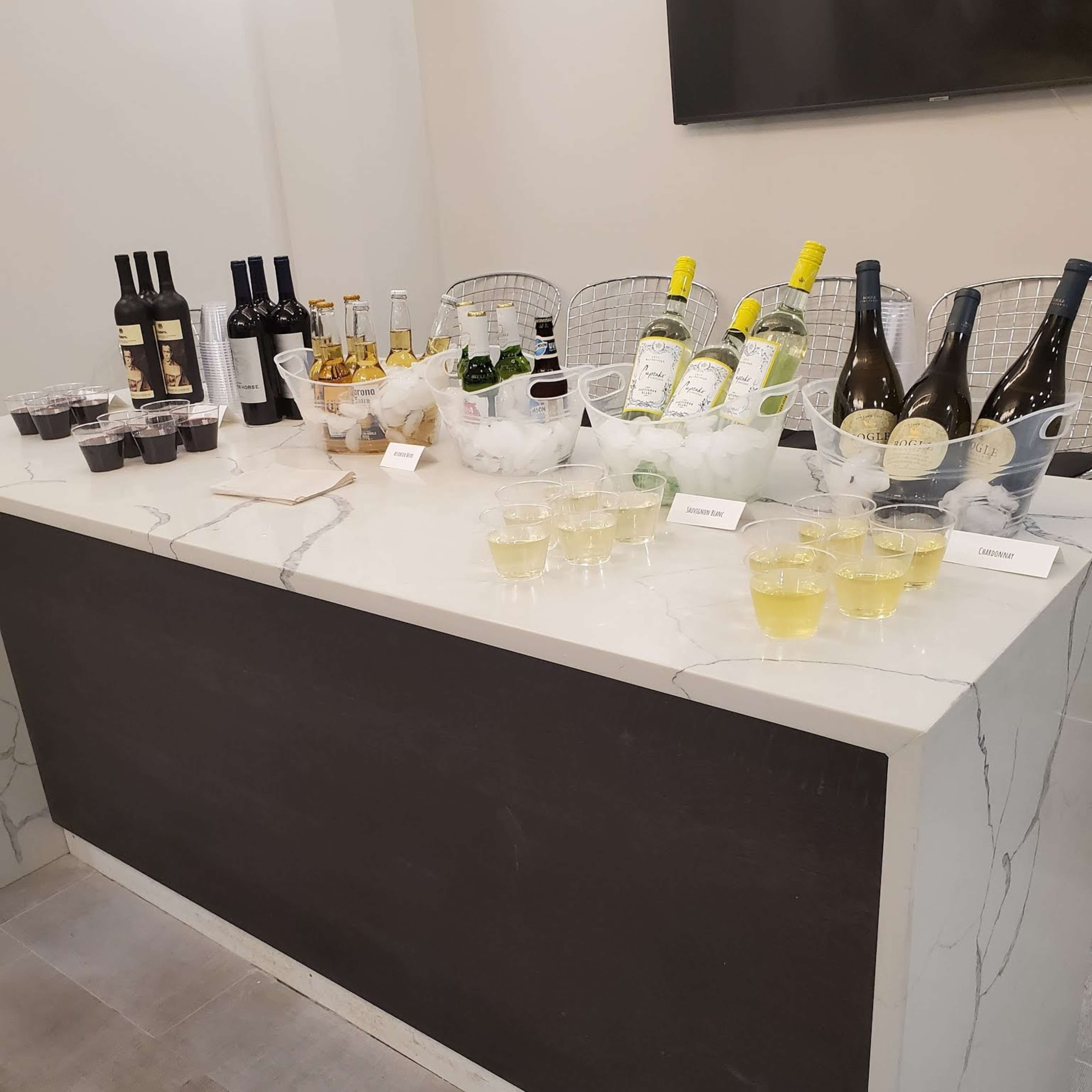A bar counter displays various bottles of wine and spirits alongside cups filled with drinks.