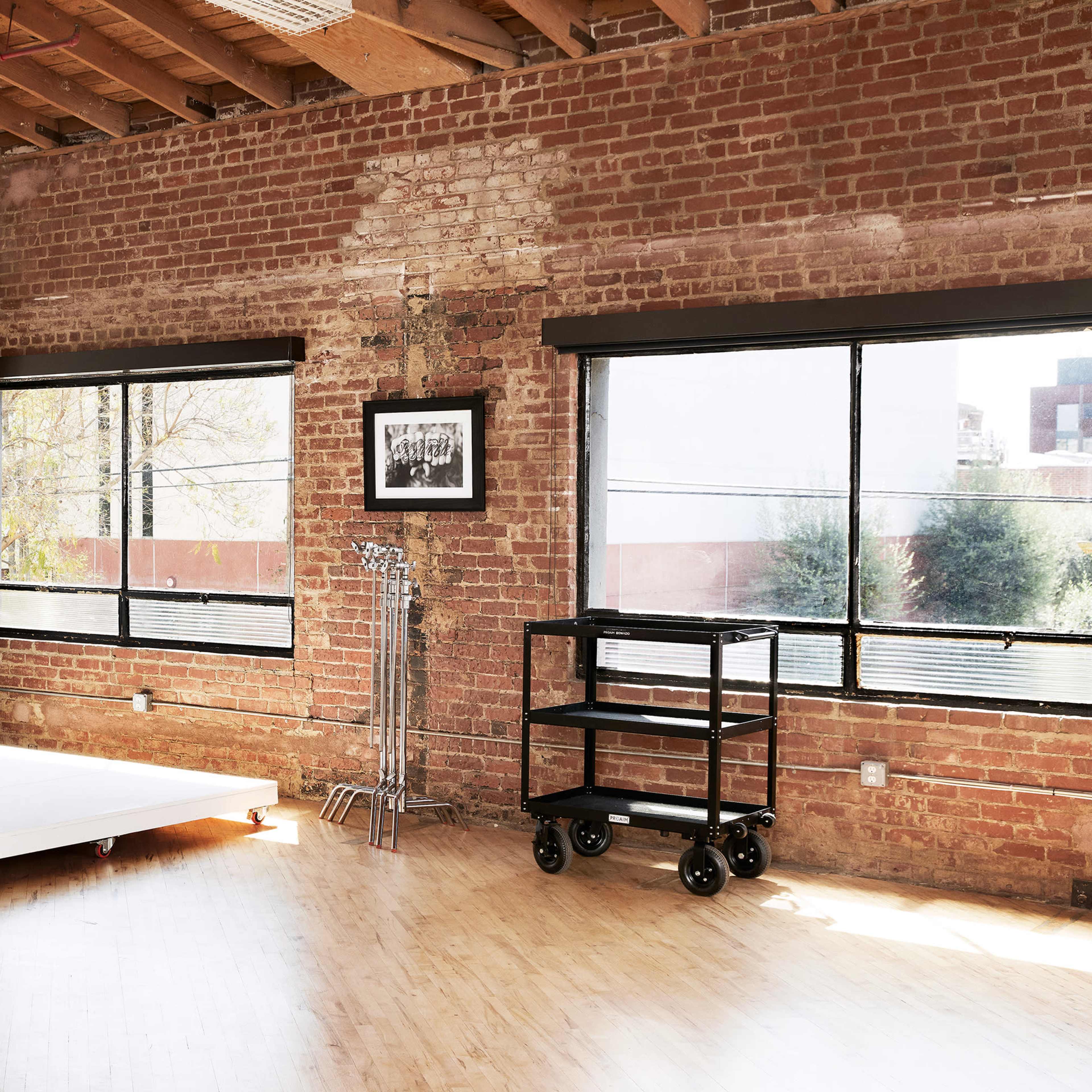 A studio space with a white backdrop, brick walls, large windows, and a rolling cart in the corner.