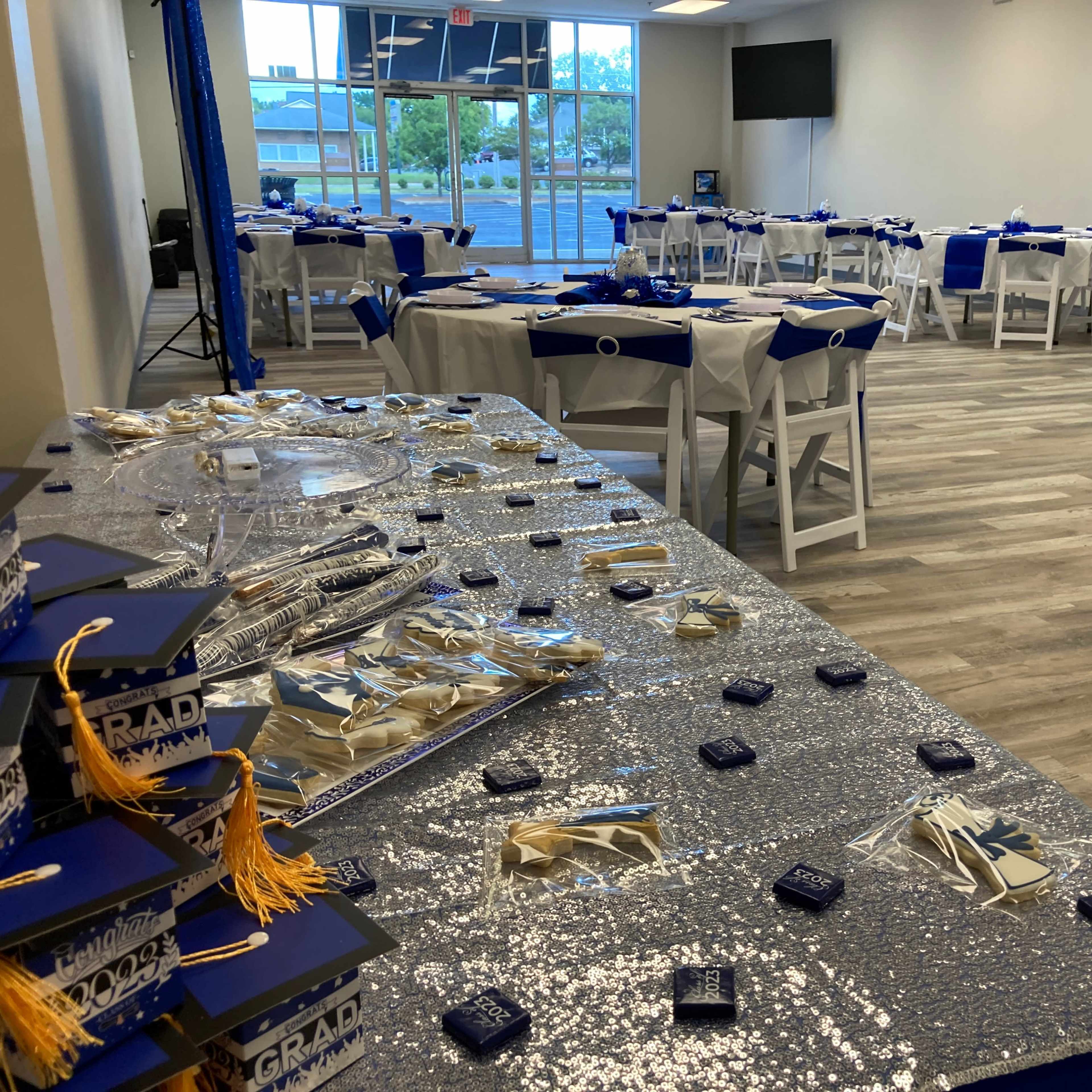 A decorated event space with tables set for a graduation celebration, featuring blue and silver decor and a display of graduation caps.