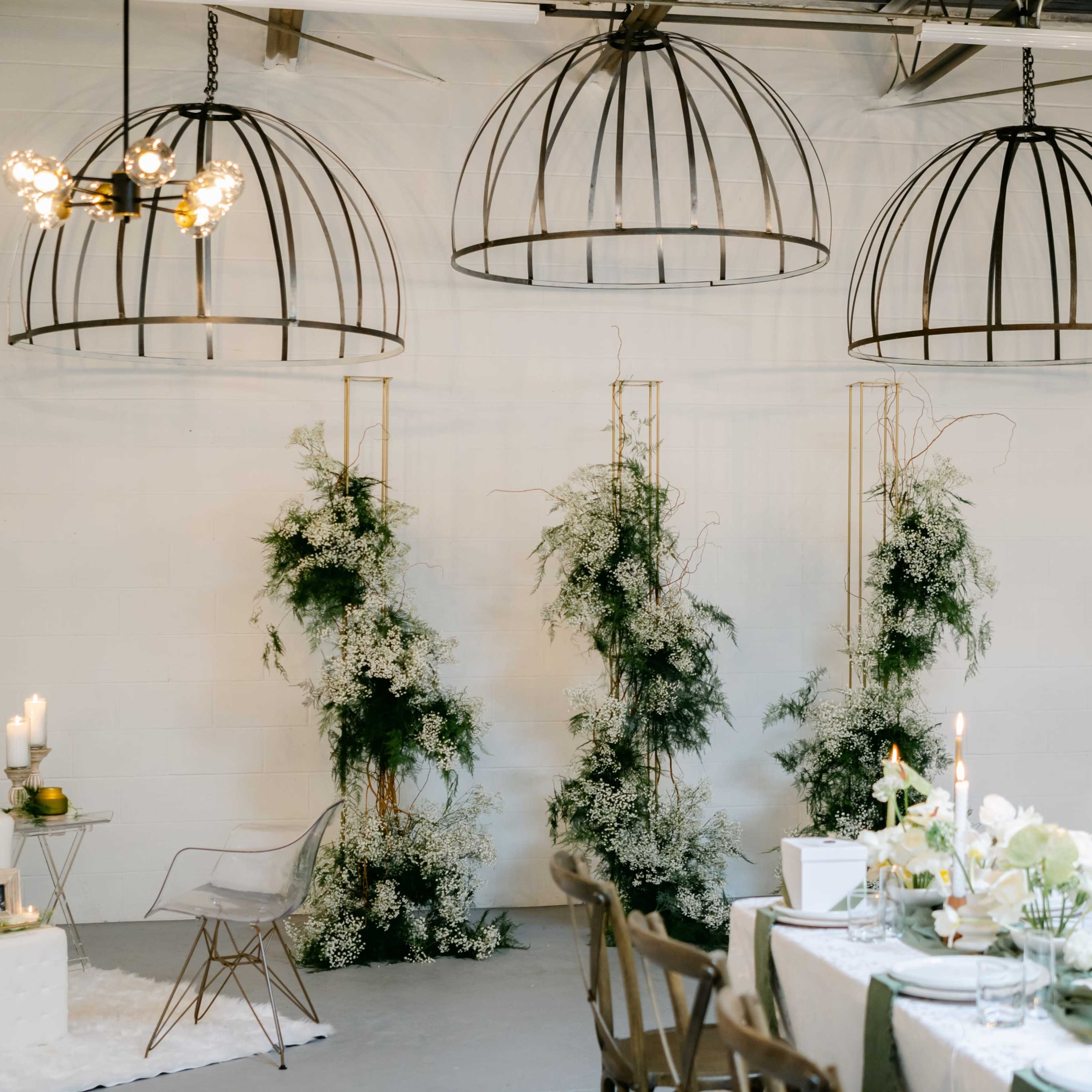 A spacious room featuring decorative hanging light fixtures, white walls, and elegantly arranged tables adorned with floral centerpieces.