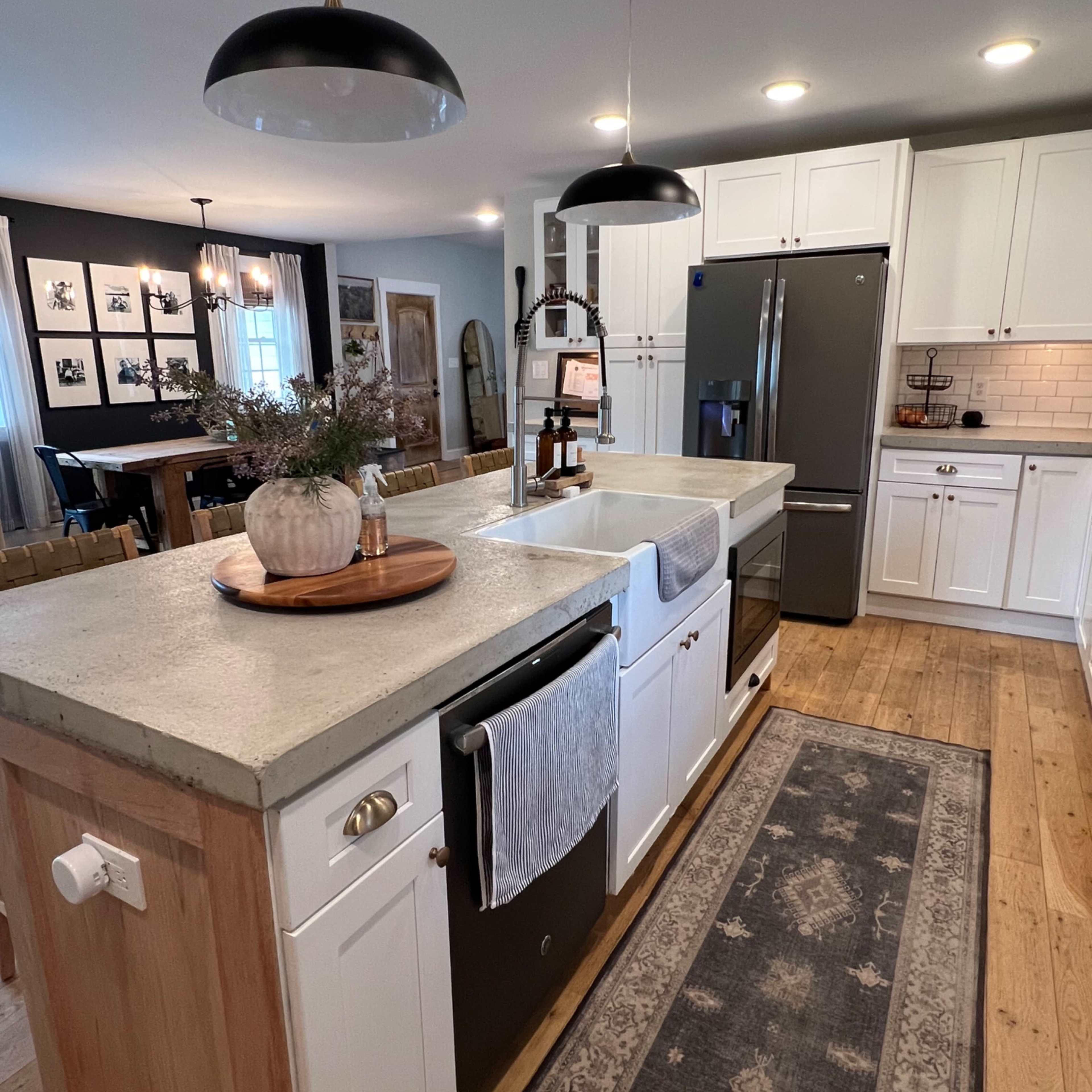 A modern kitchen features a central island with a concrete countertop, white cabinetry, and stainless steel appliances.