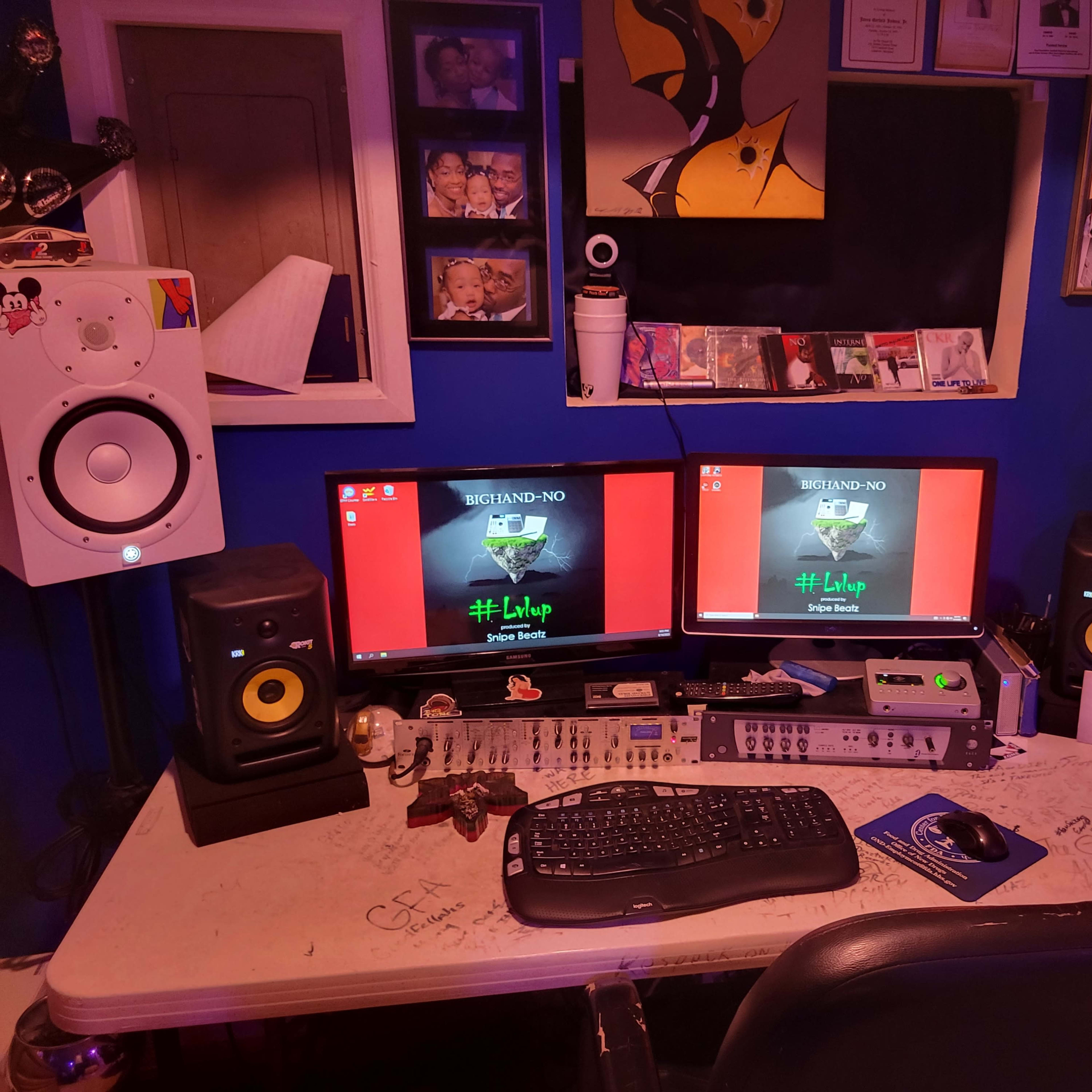 A workstation with two computer monitors, studio speakers, a keyboard, and audio equipment in a blue-walled room filled with various decorations and personal items.