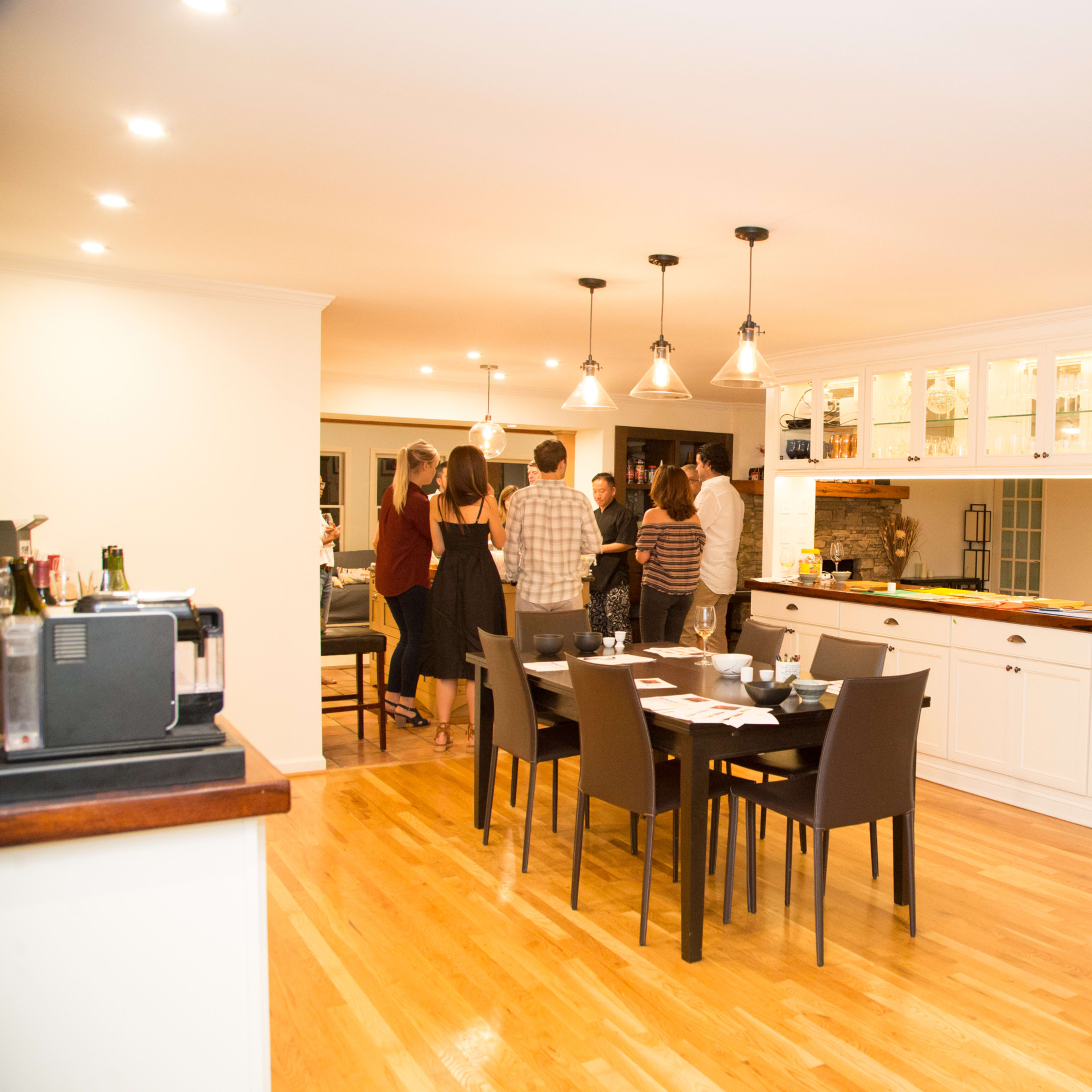 A group of people stands around a kitchen island in a modern, open-concept dining area.