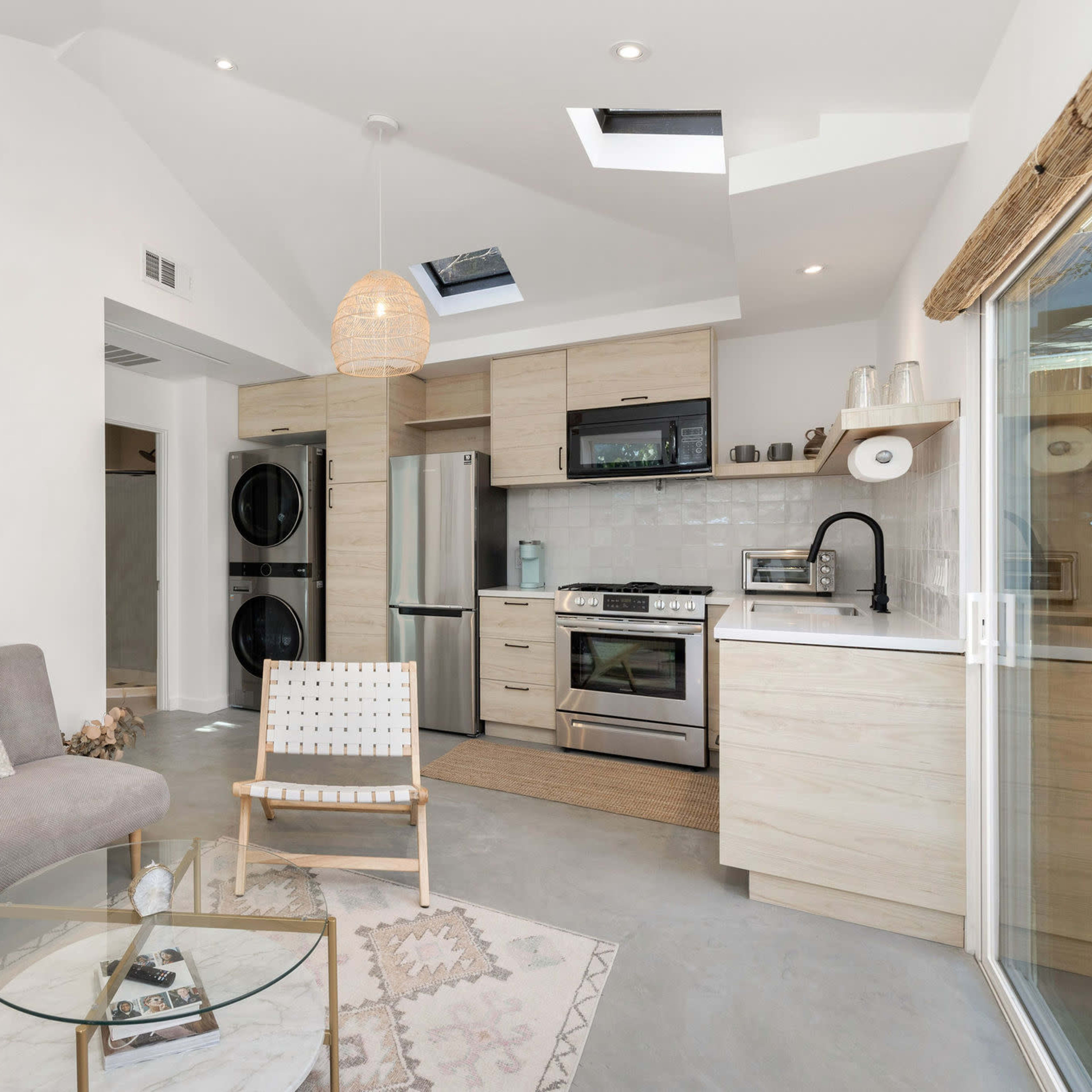A modern living space featuring a light-colored sofa, a round glass coffee table, and a kitchen area with stainless steel appliances.