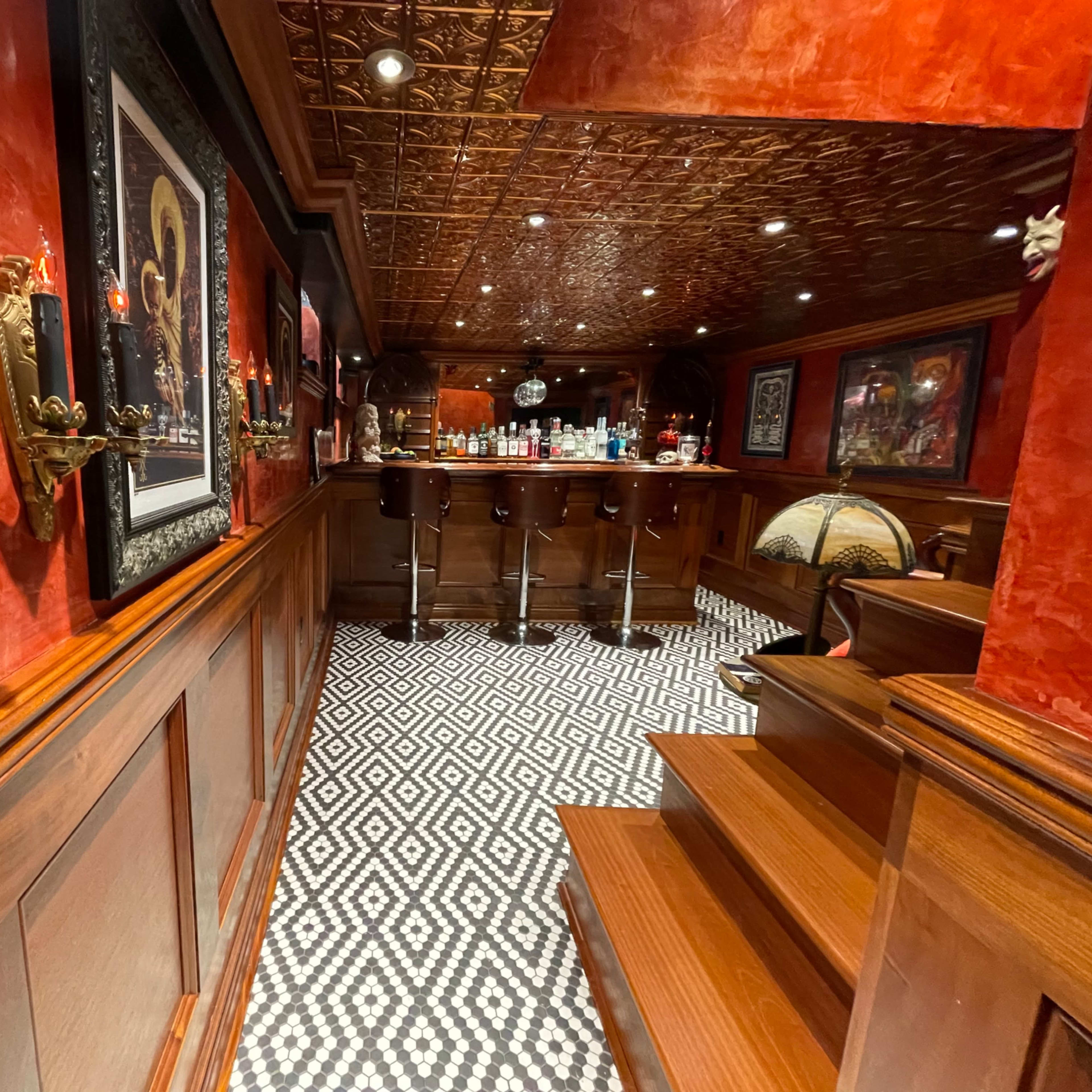 An upscale bar area with dark wood paneling, patterned tile flooring, and a well-stocked backlit bar.