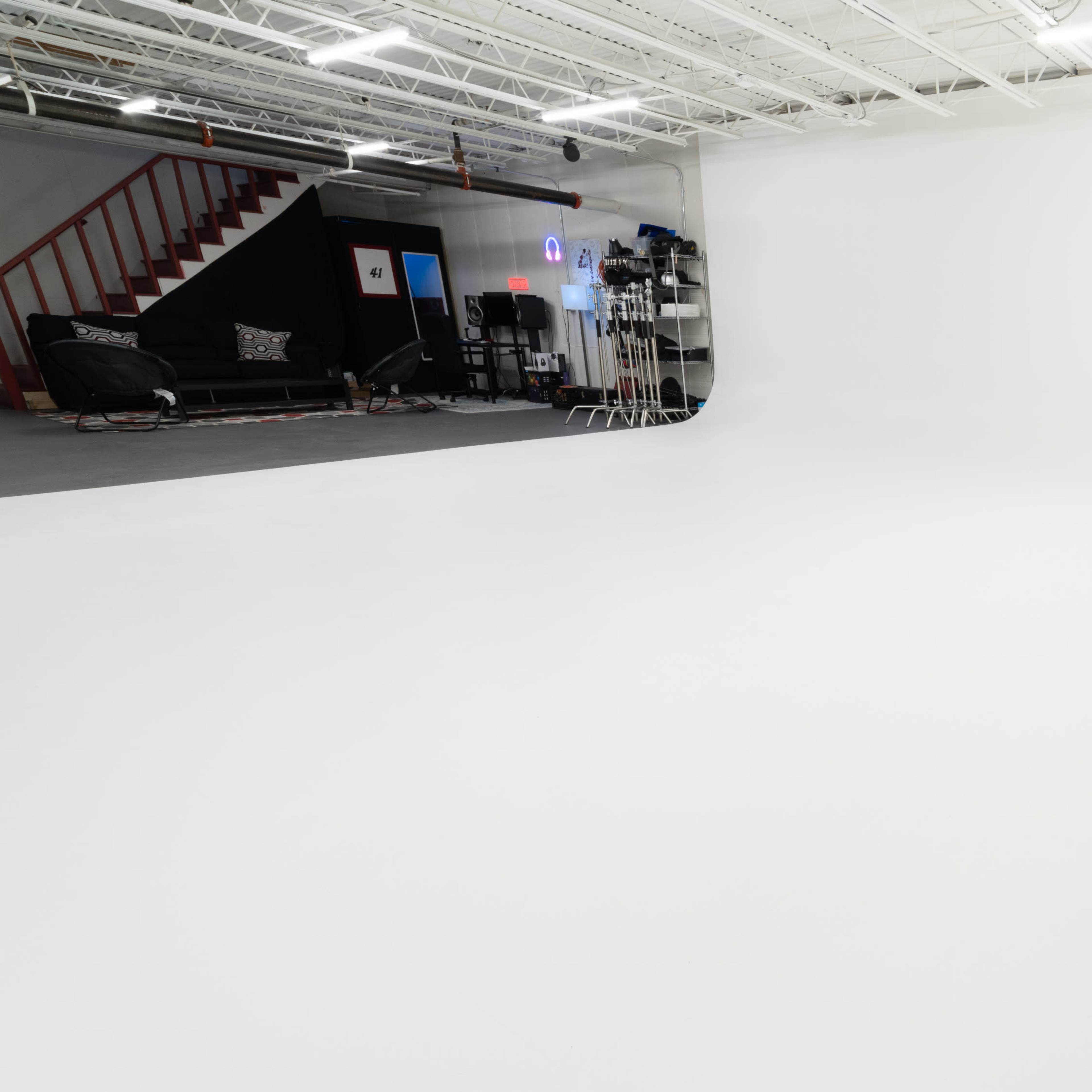 A large, empty studio space with a seamless white backdrop and various filmmaking equipment visible in the background.