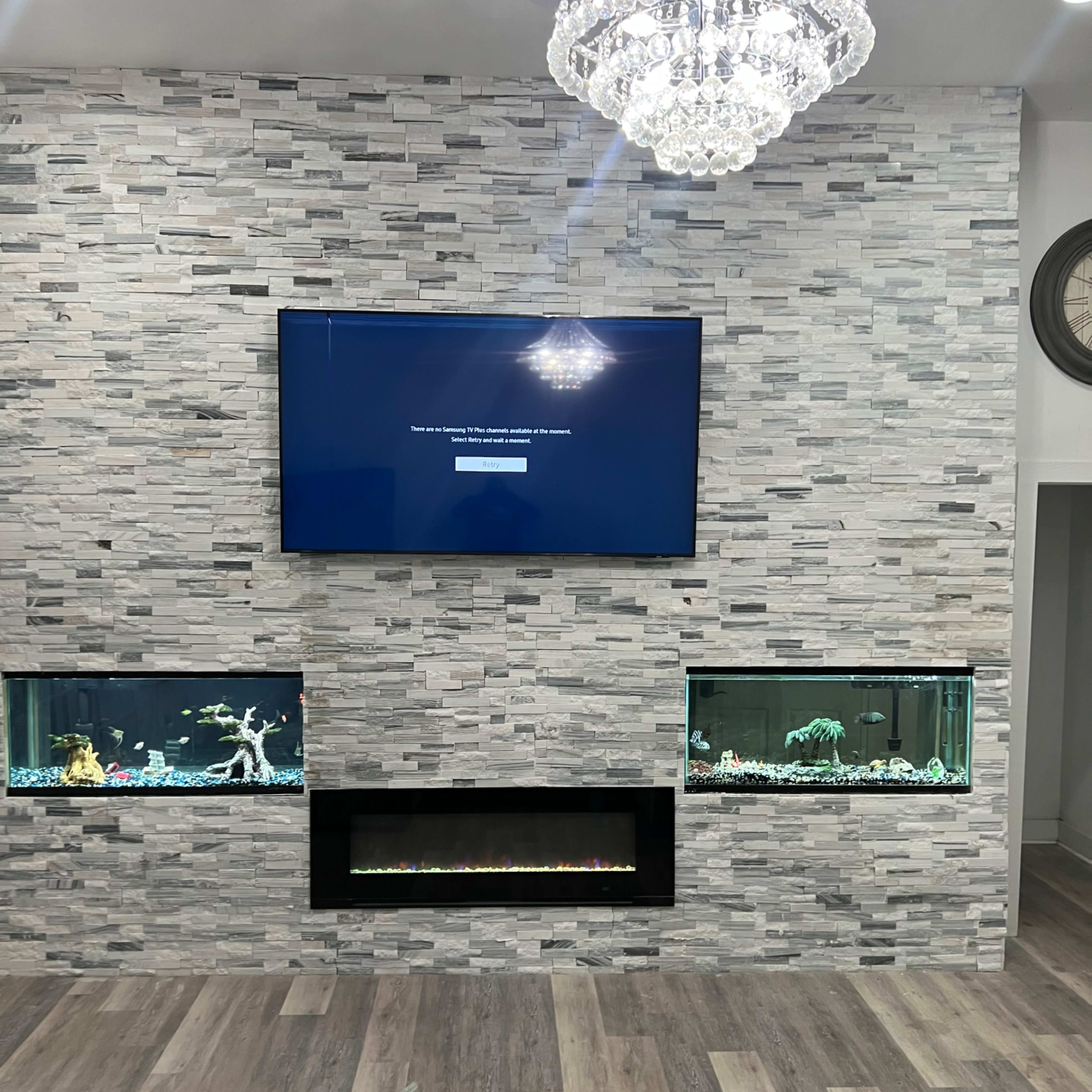 A modern living room features a gray stone wall with a television mounted above a sleek electric fireplace, flanked by two built-in aquariums.