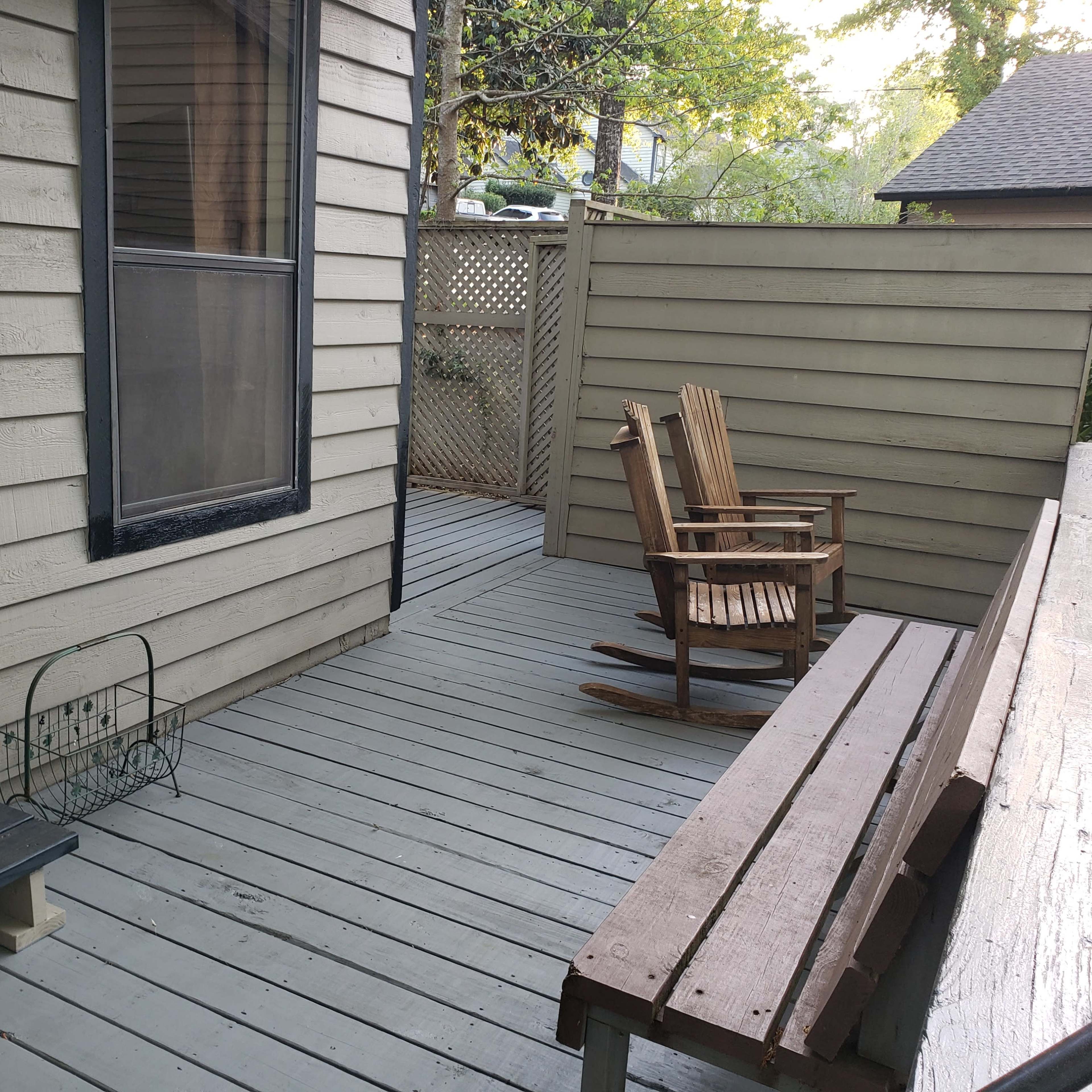 A wooden deck with a pair of rocking chairs and a long bench alongside a house.