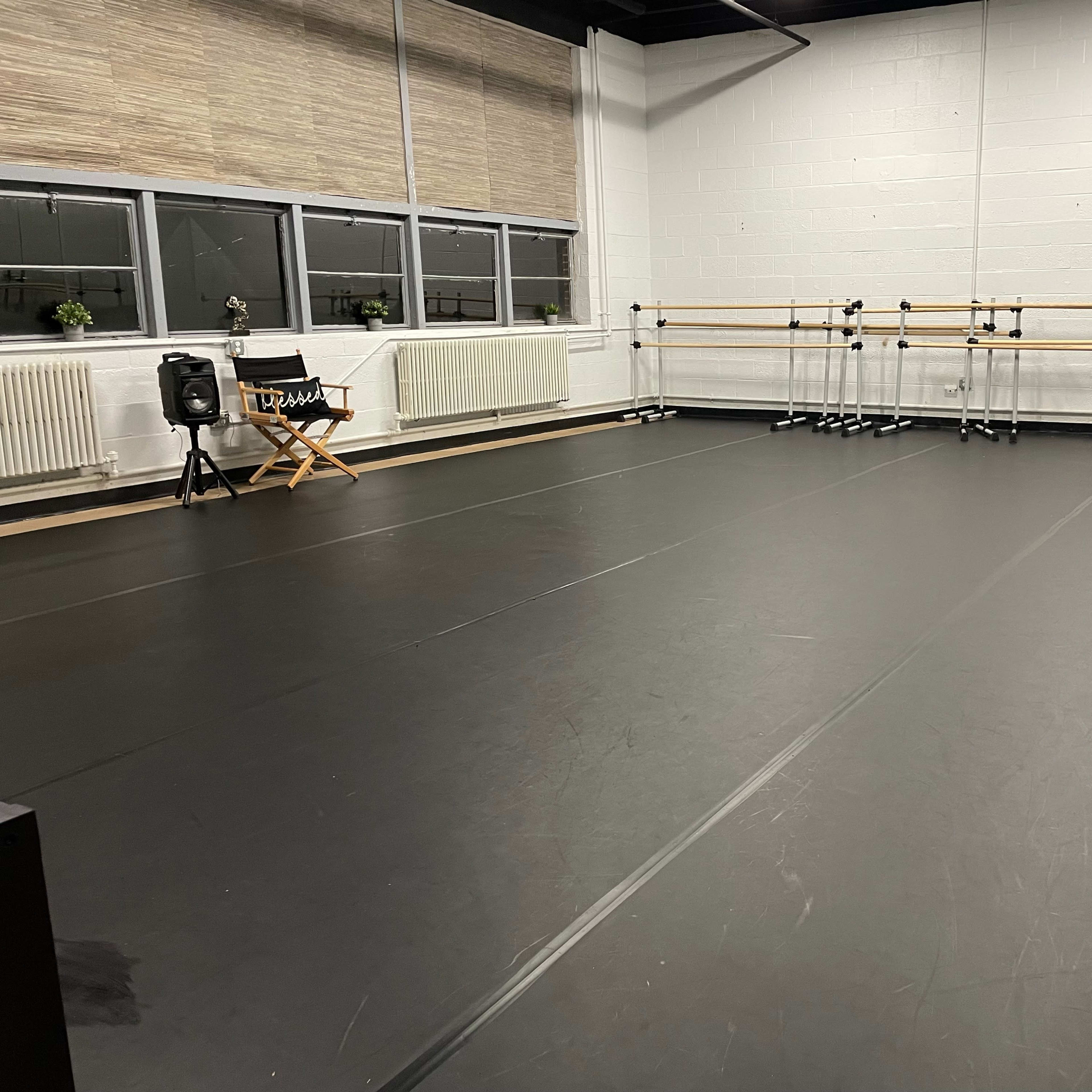 A spacious dance studio with a black floor, wall mirrors, and wooden ballet barres along one side.