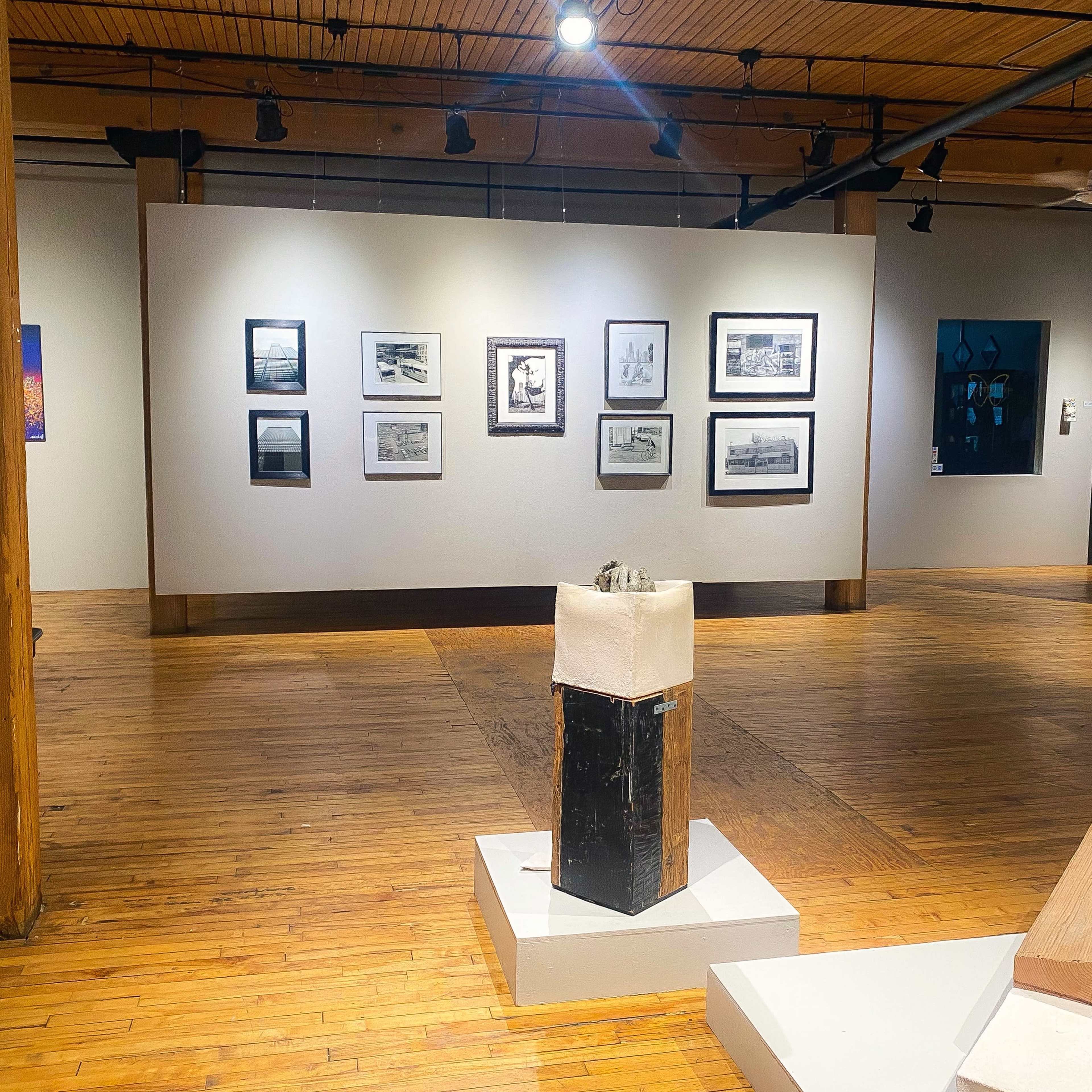 An art gallery with framed photographs hanging on the walls and a sculpture displayed on a pedestal in the center.