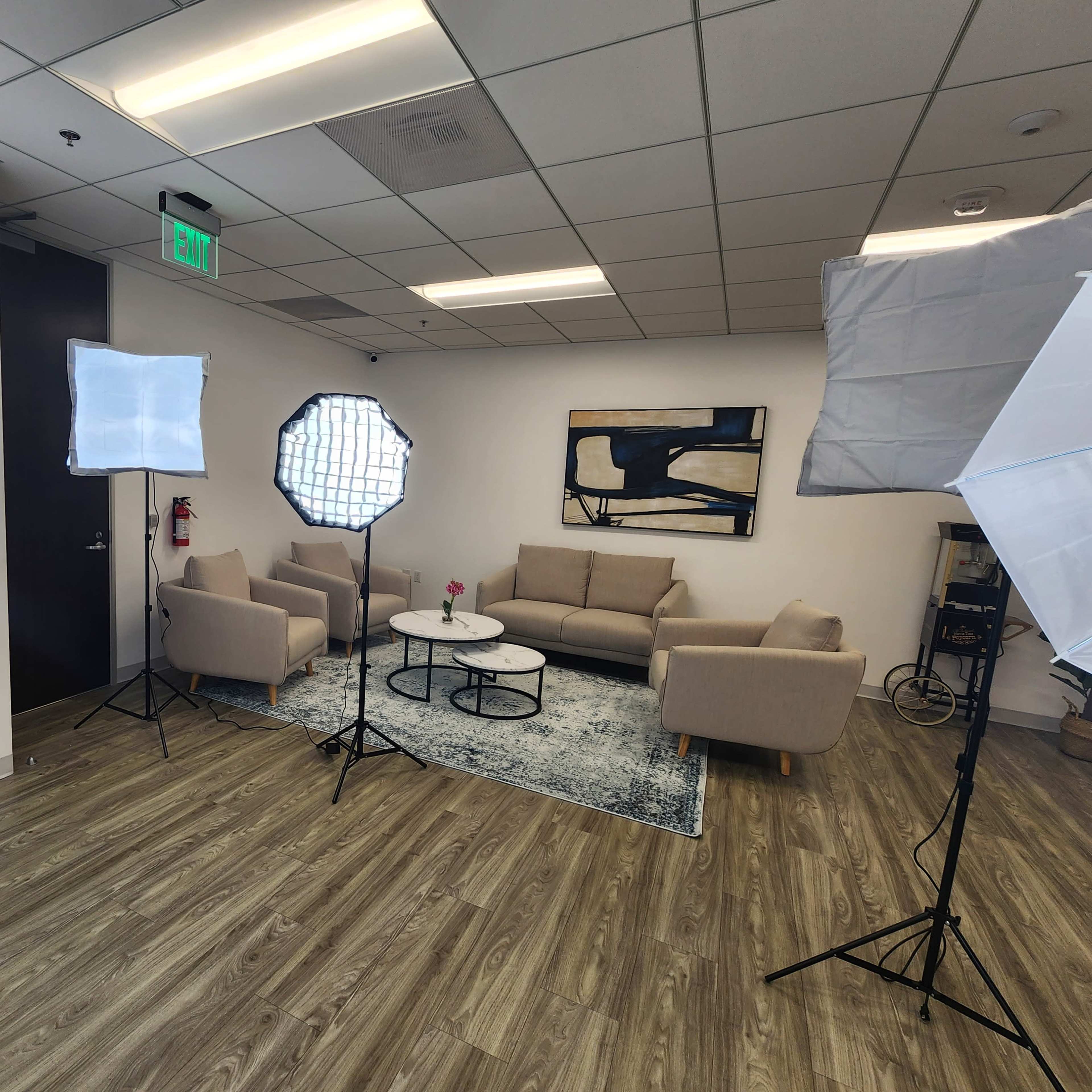 A well-lit indoor lounge area with a sofa, coffee table, and a decorative flower, surrounded by photography lighting equipment.