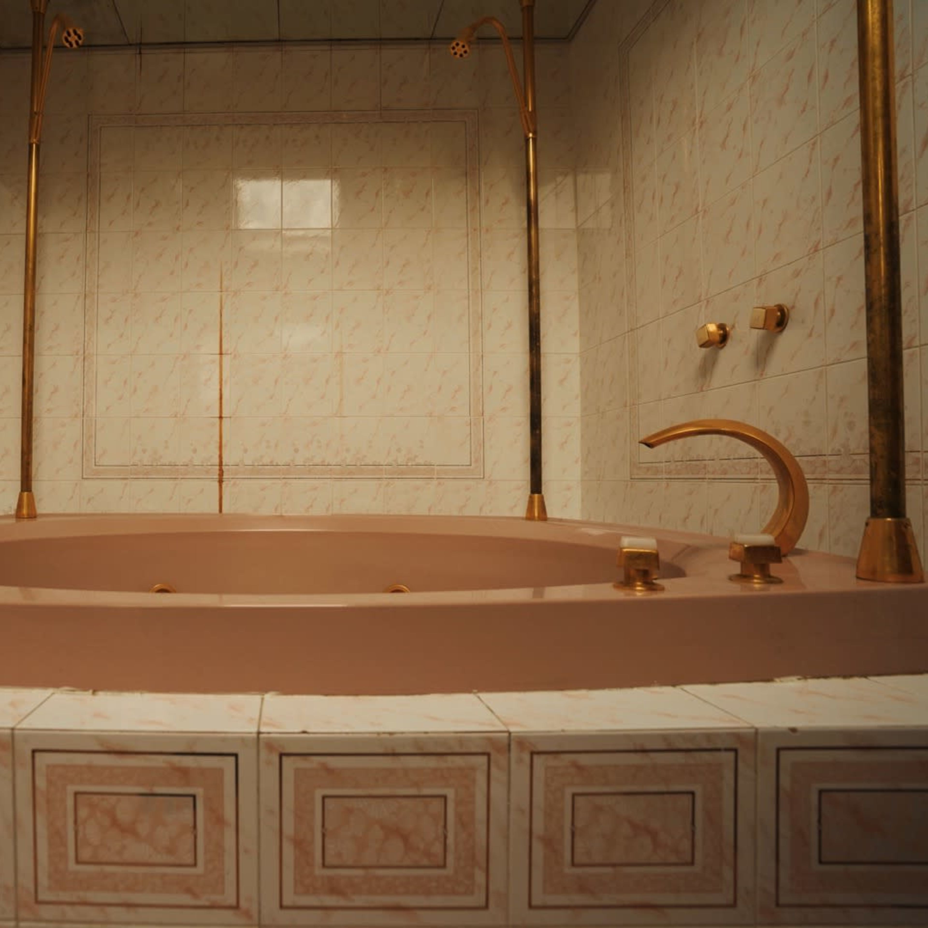 A spacious bathtub with gold fixtures set against pale marble-patterned tiles.