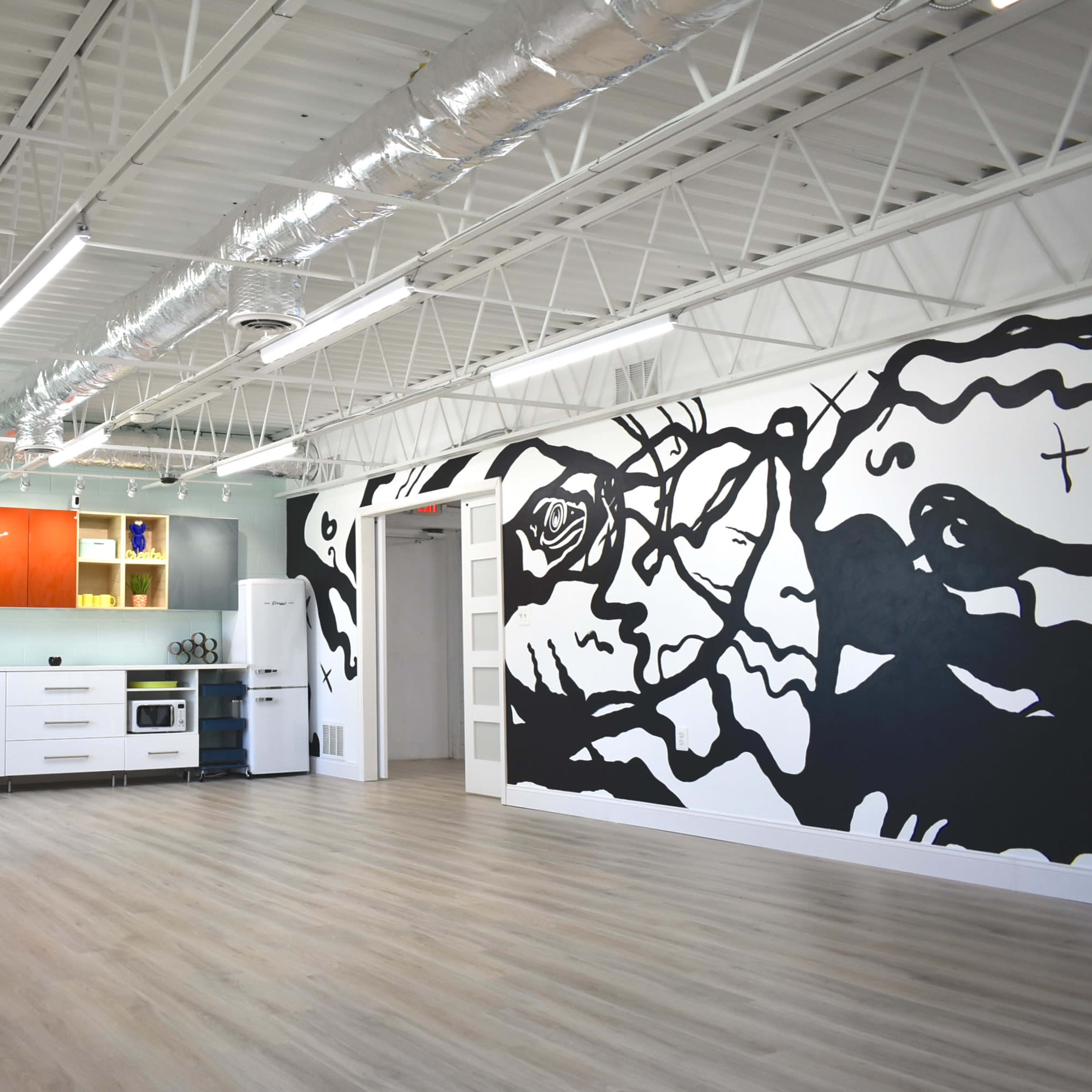 A spacious, modern room featuring a kitchen area with colorful cabinets and a large black mural on one wall.