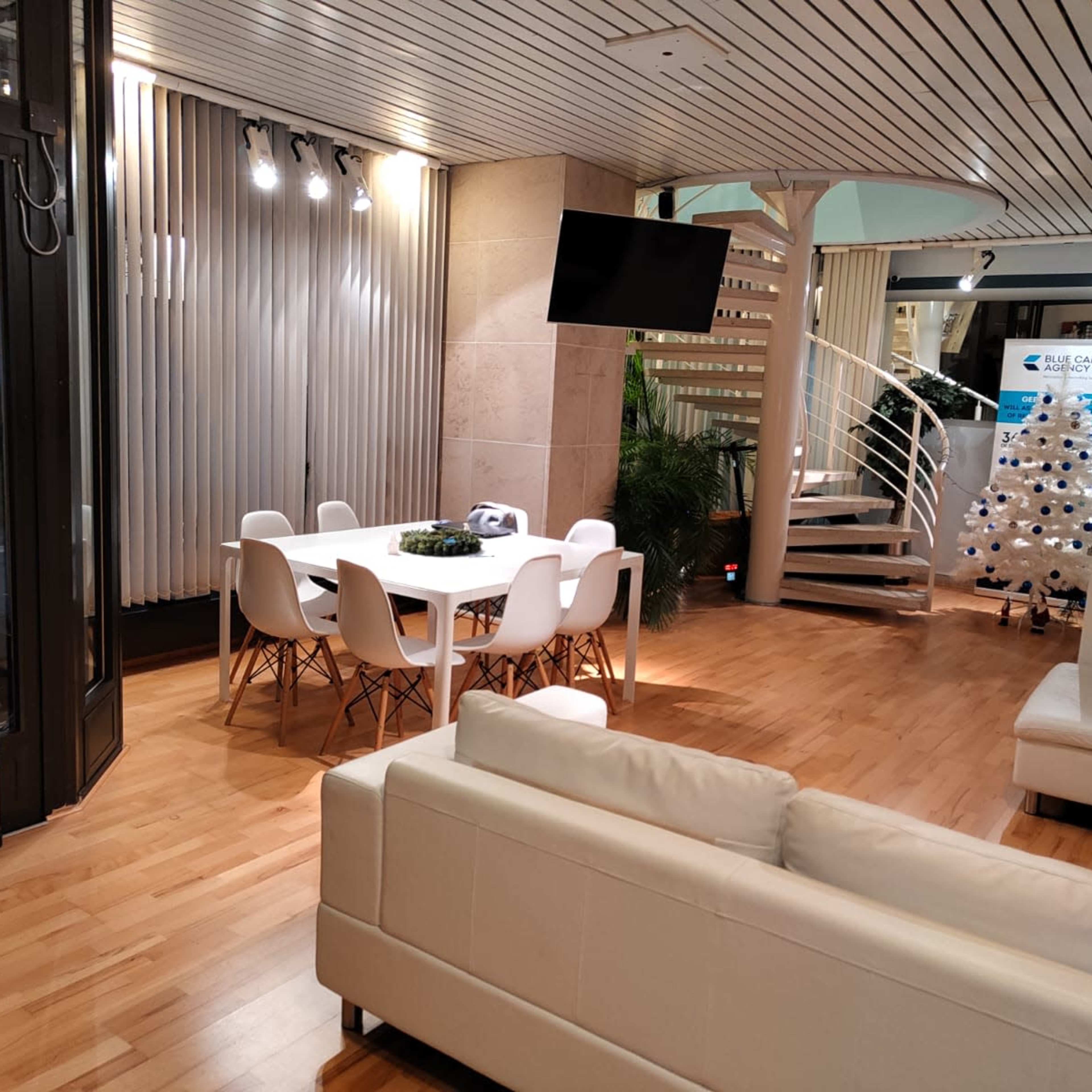 A modern interior space featuring a dining area with a white table and chairs, a seating area with a white sofa, and a spiral staircase leading to an upper level.