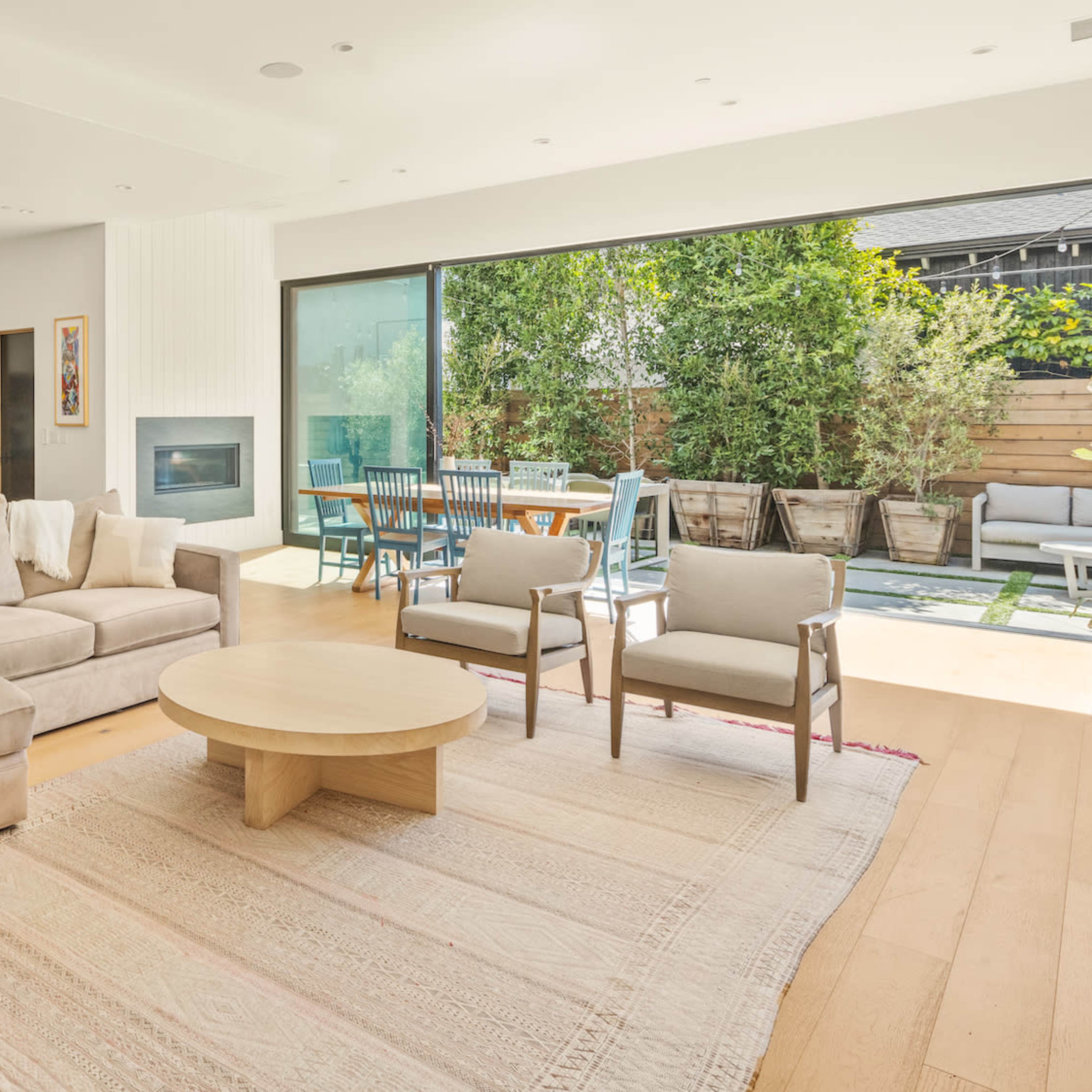 A modern living room features a light-colored sectional sofa, a round coffee table, and large sliding glass doors leading to an outdoor patio area.