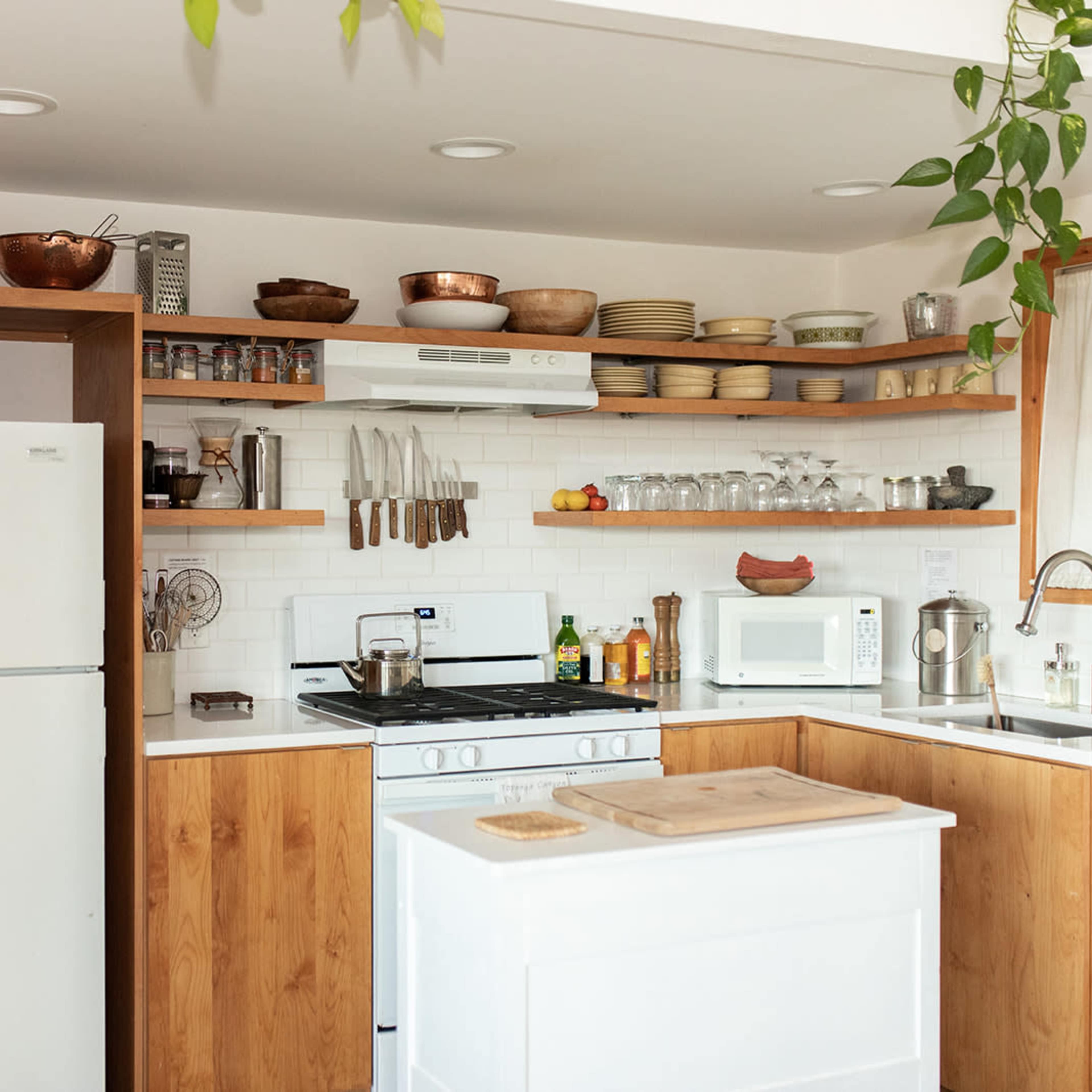 A modern kitchen with wooden cabinetry, a white refrigerator, a gas stove, and open shelves displaying various kitchenware and plants.