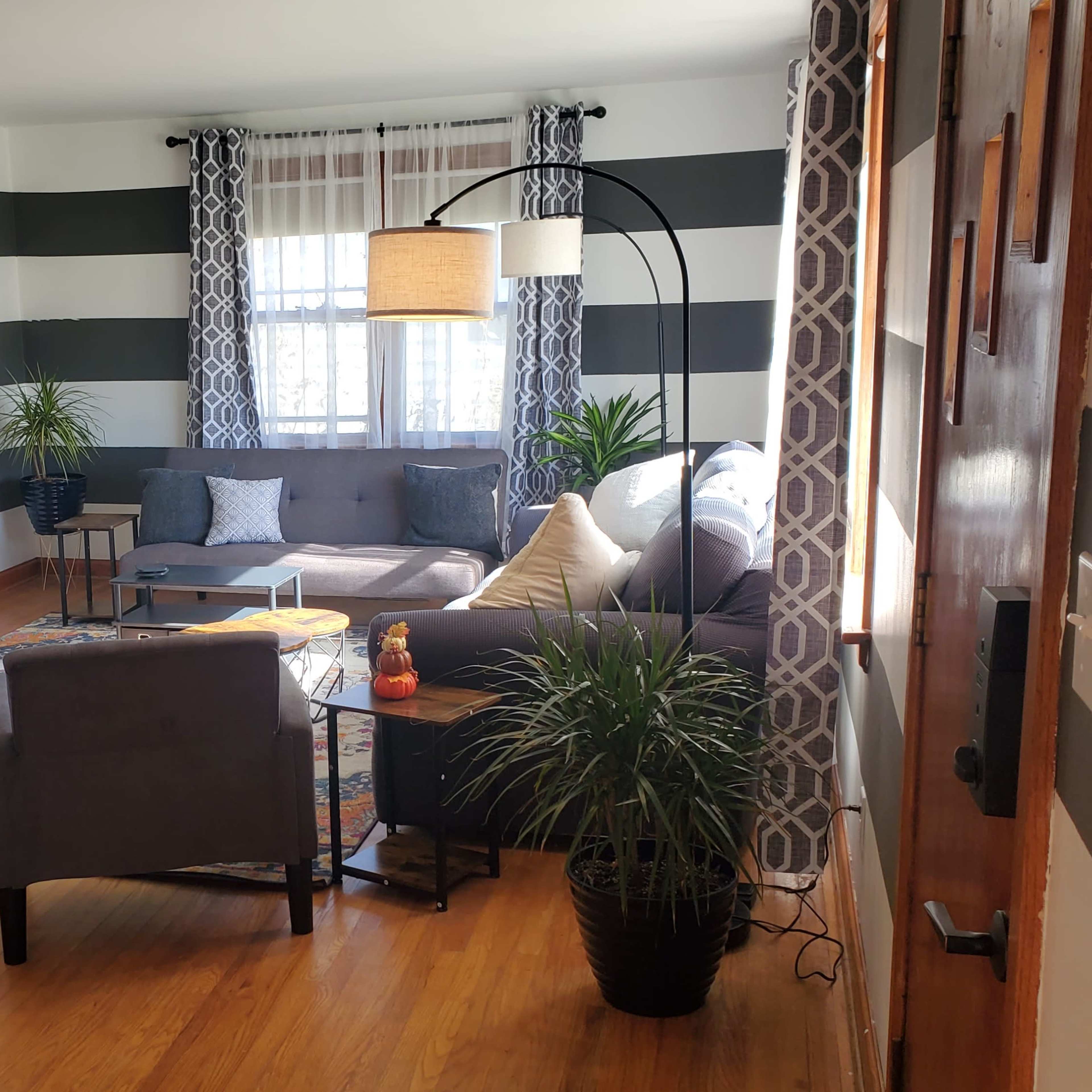 A modern living room with striped walls, a large television, two armchairs, a sofa, and decorative plants.