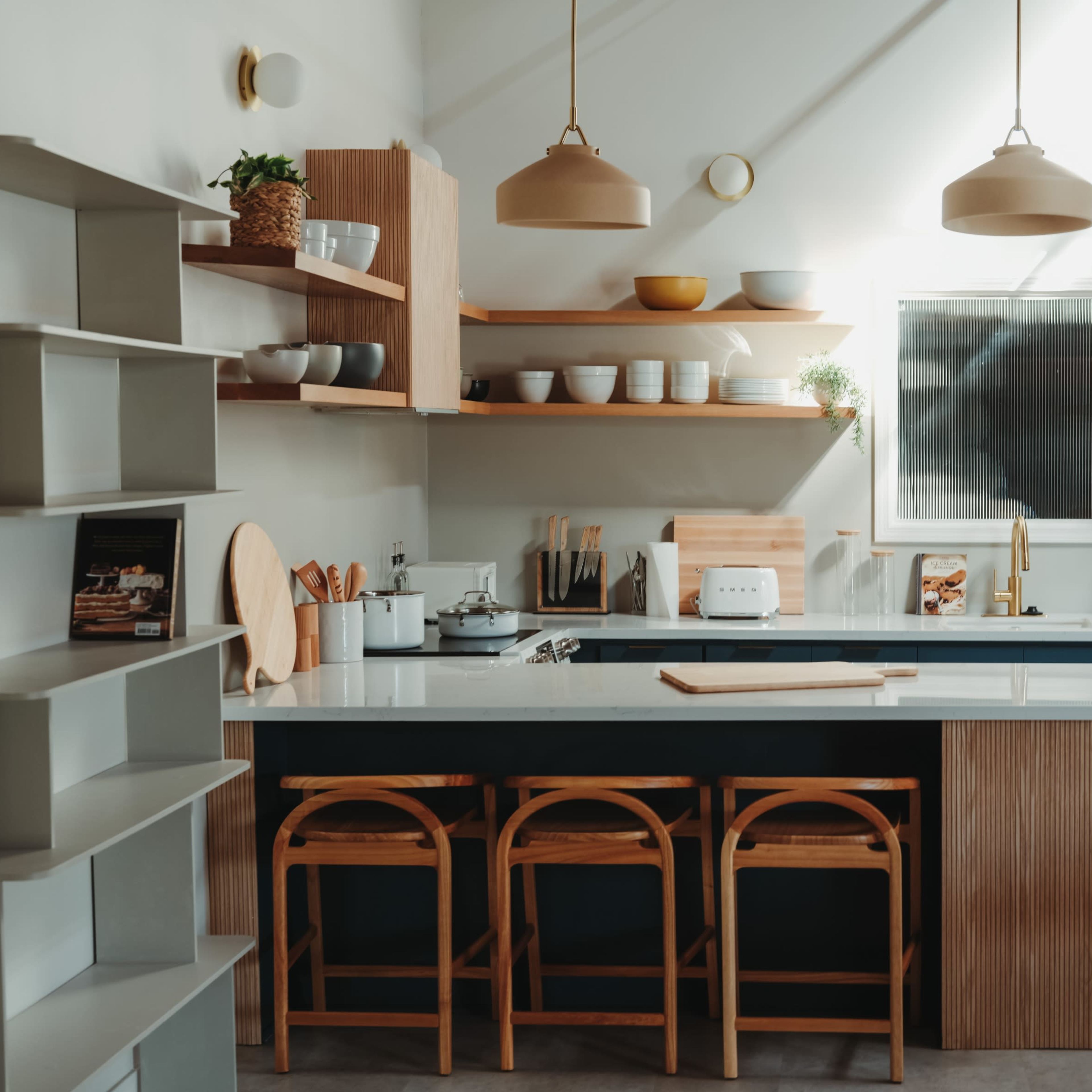 A modern kitchen features a blue and wooden color scheme with open shelving, pendant lights, and bar stools around an island.
