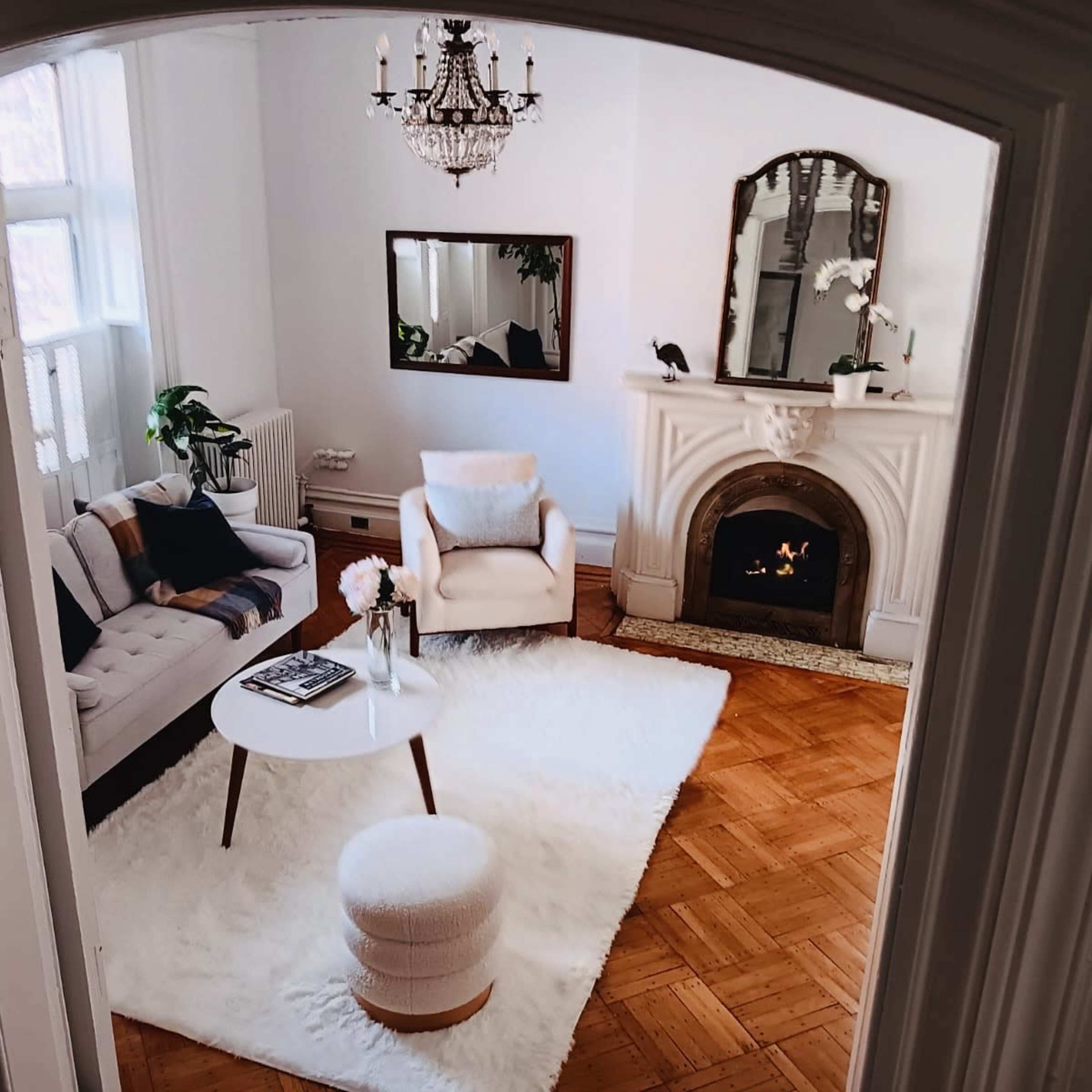 A bright living room featuring a light-colored sofa, a small round table, a plush rug, and a decorative fireplace.