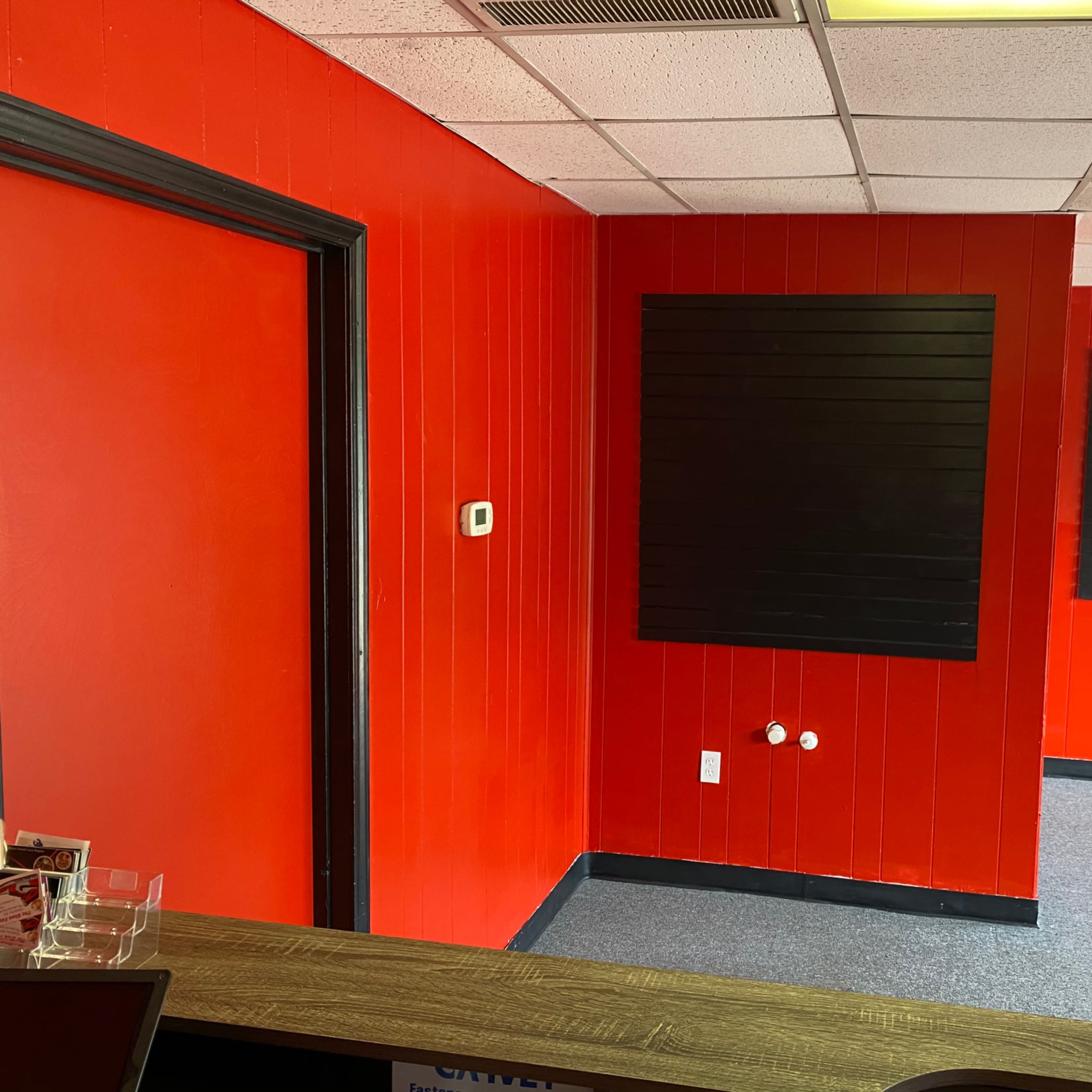 A room with bright red walls, a dark black wall panel, and a gray carpeted floor.