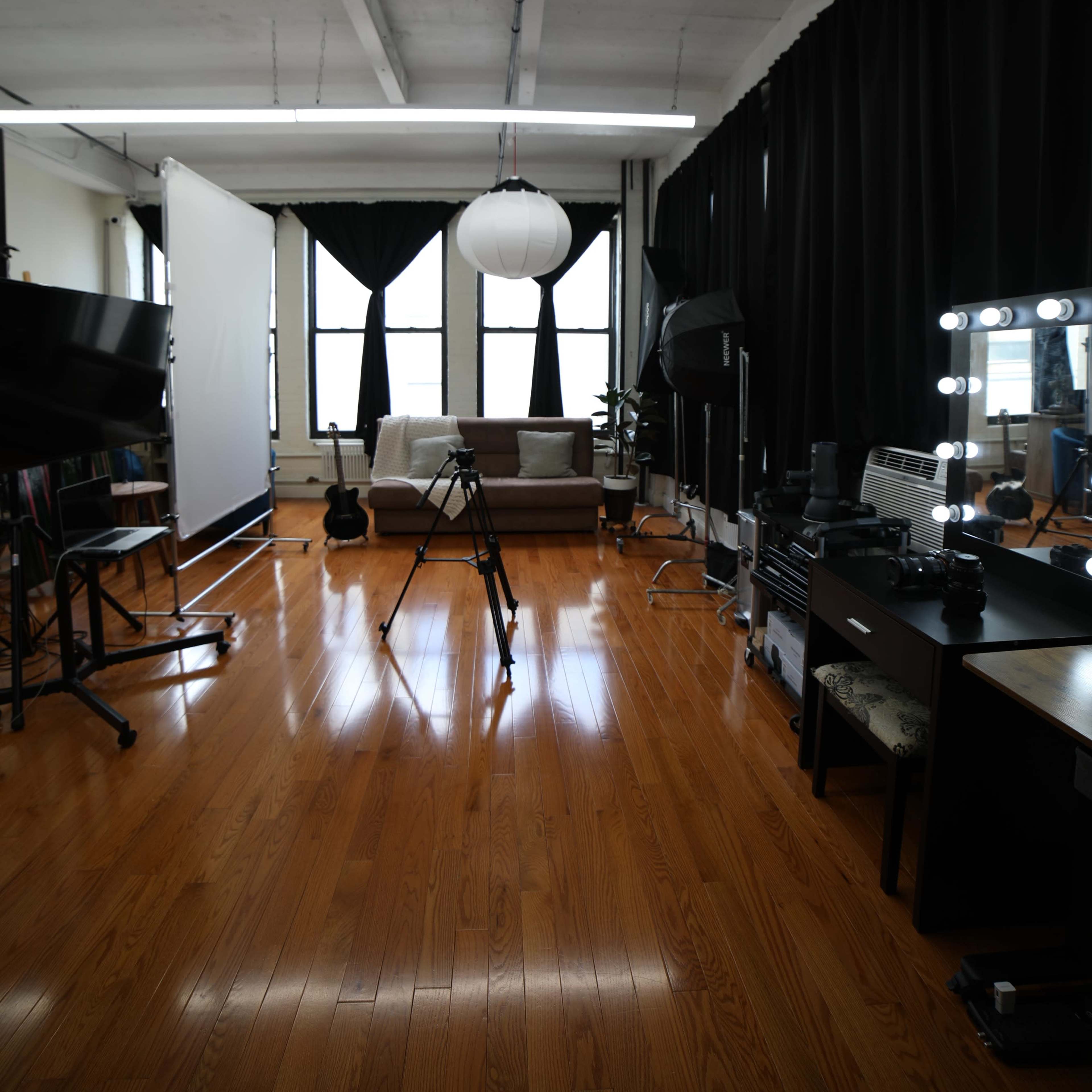 A well-equipped photography studio featuring a tripod, lighting equipment, a large white backdrop, and a comfortable seating area.