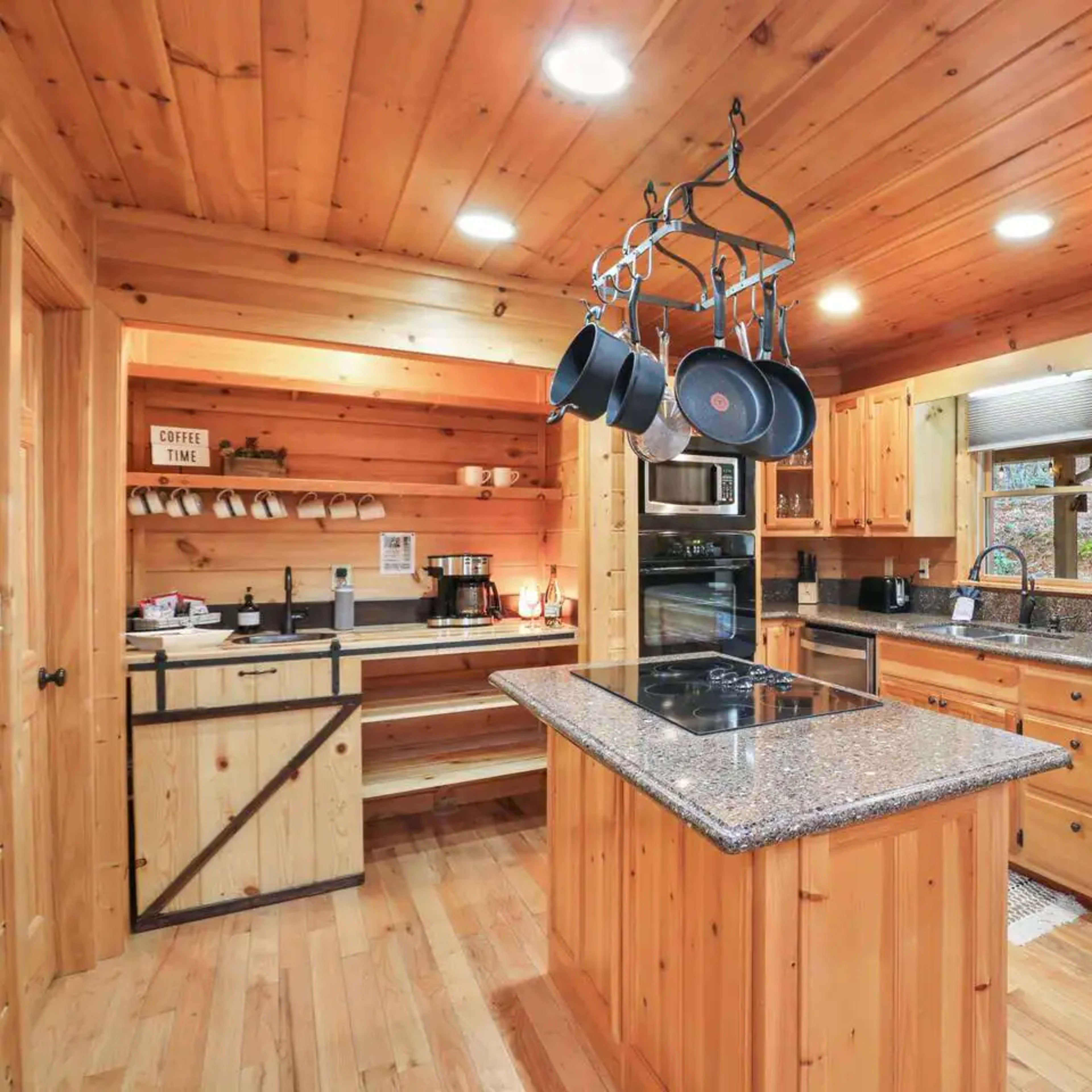The kitchen features wooden cabinets, a central island with a stove, and stainless steel appliances under bright overhead lighting.
