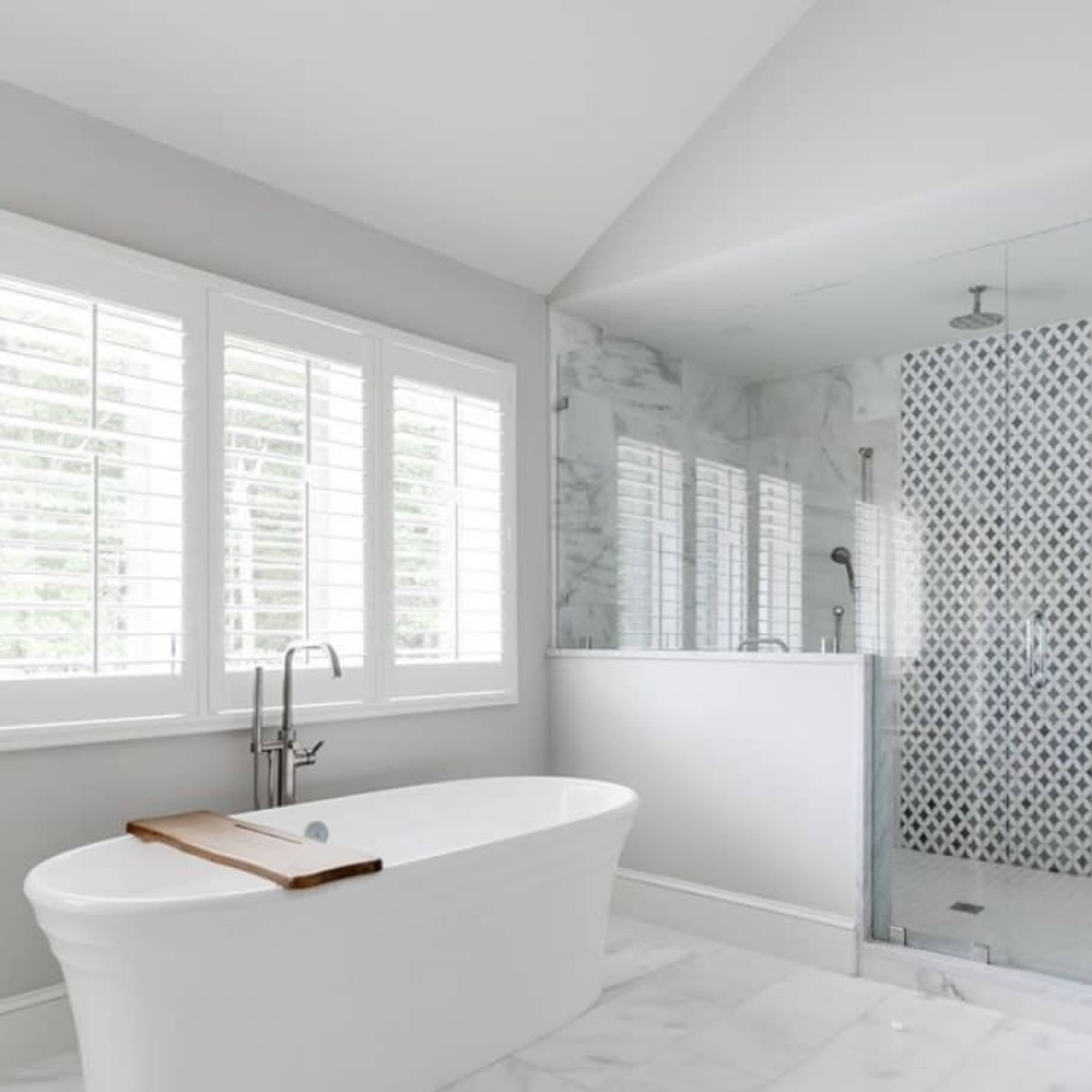A modern bathroom features a freestanding white bathtub and a glass shower with a patterned tile wall.
