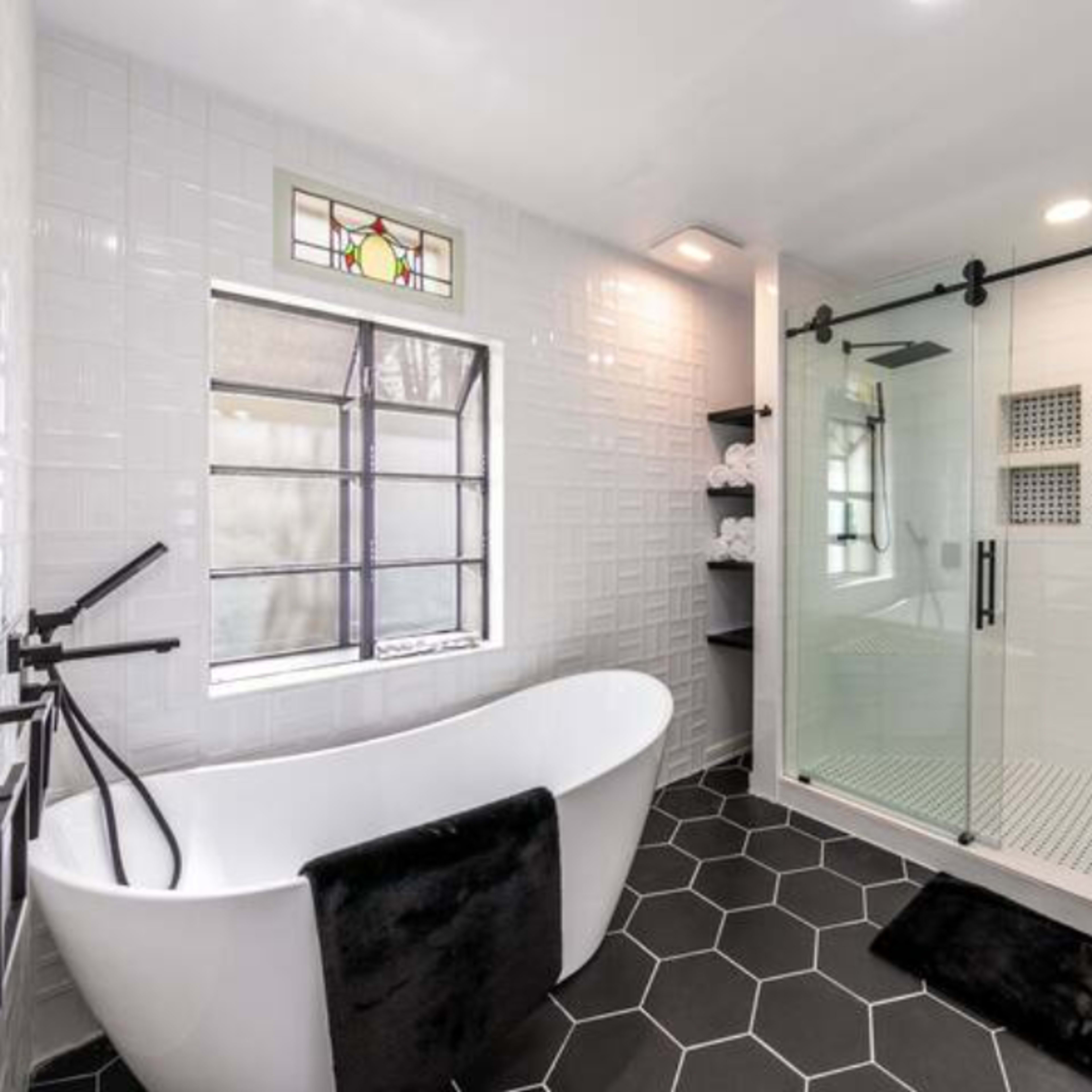 A modern bathroom featuring a freestanding bathtub, a glass shower enclosure, and a large window.