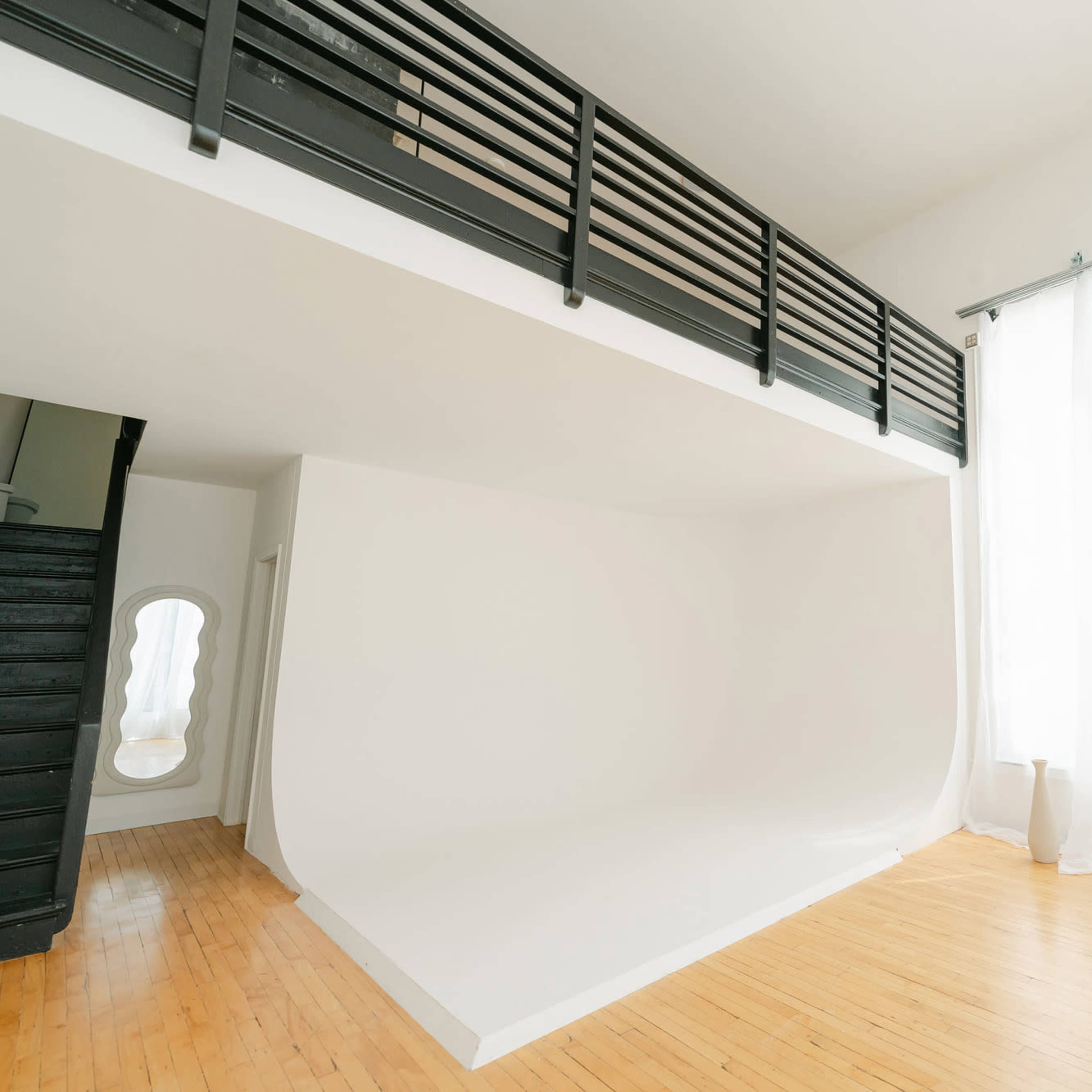 A spacious interior with a large seamless white wall, wooden flooring, and soft natural light filtering through sheer curtains.