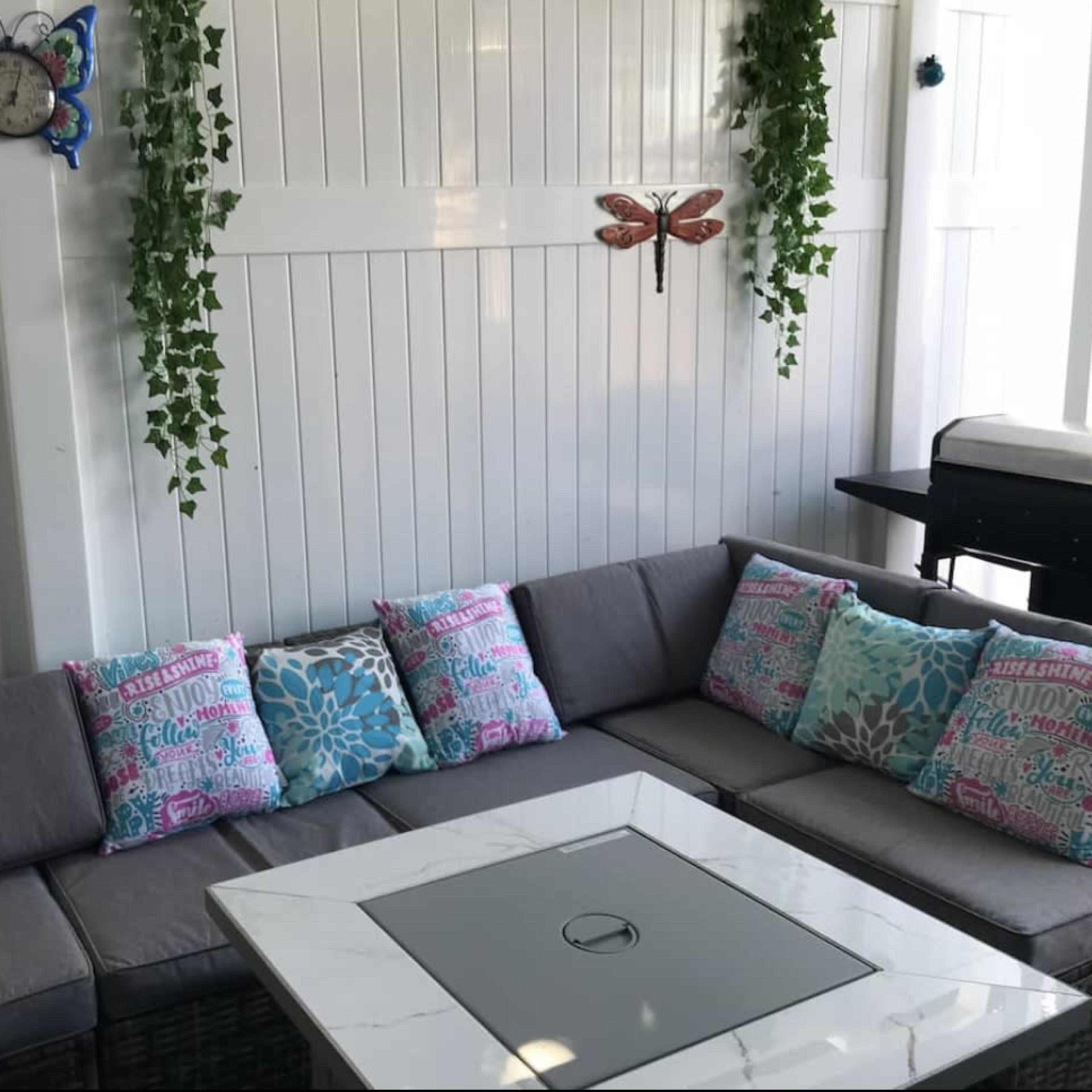 A cozy seating area with a sectional sofa adorned with colorful throw pillows, a square coffee table, and decorative wall elements including a clock and wall hangings.