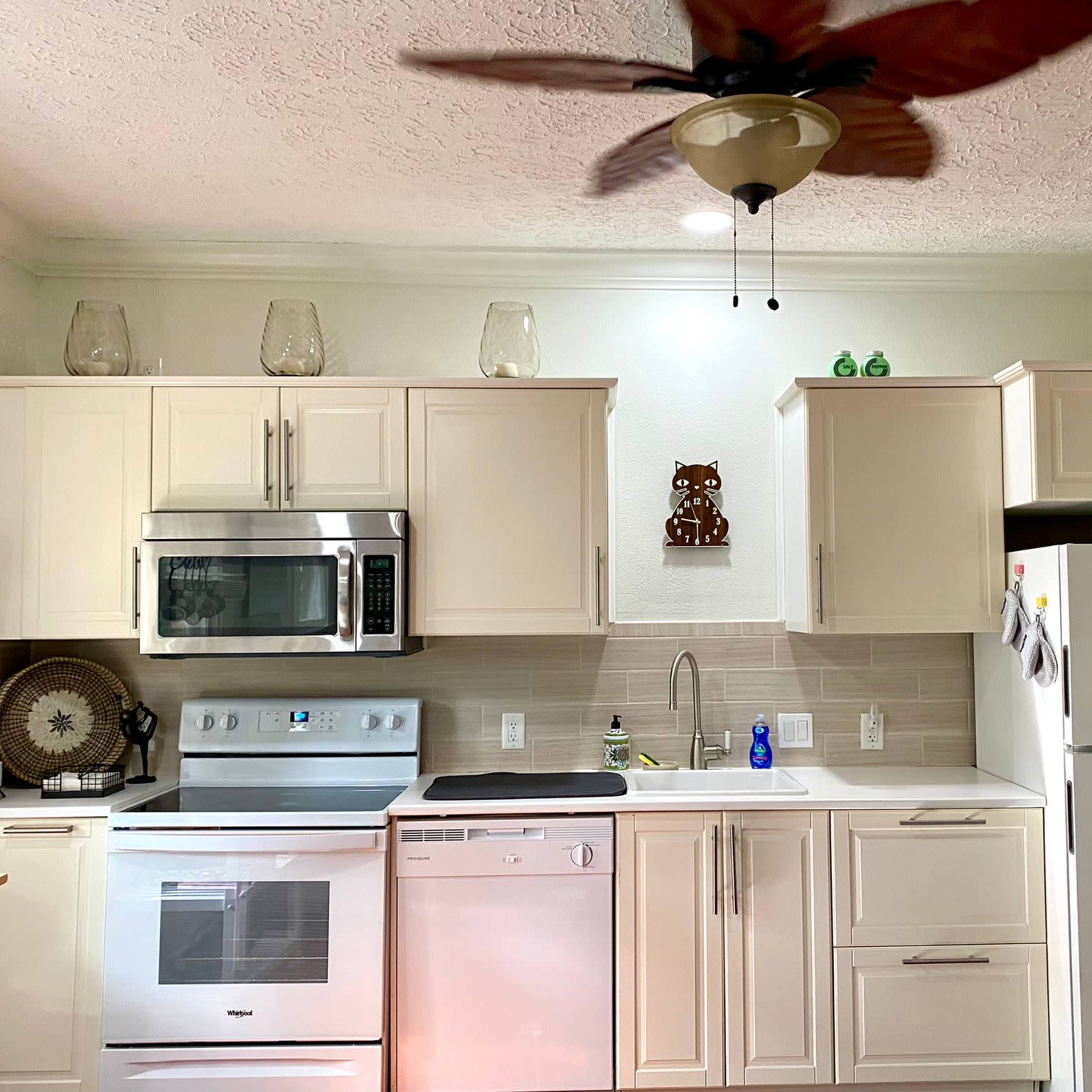 A modern kitchen features stainless steel appliances, light-colored cabinetry, and a ceiling fan.