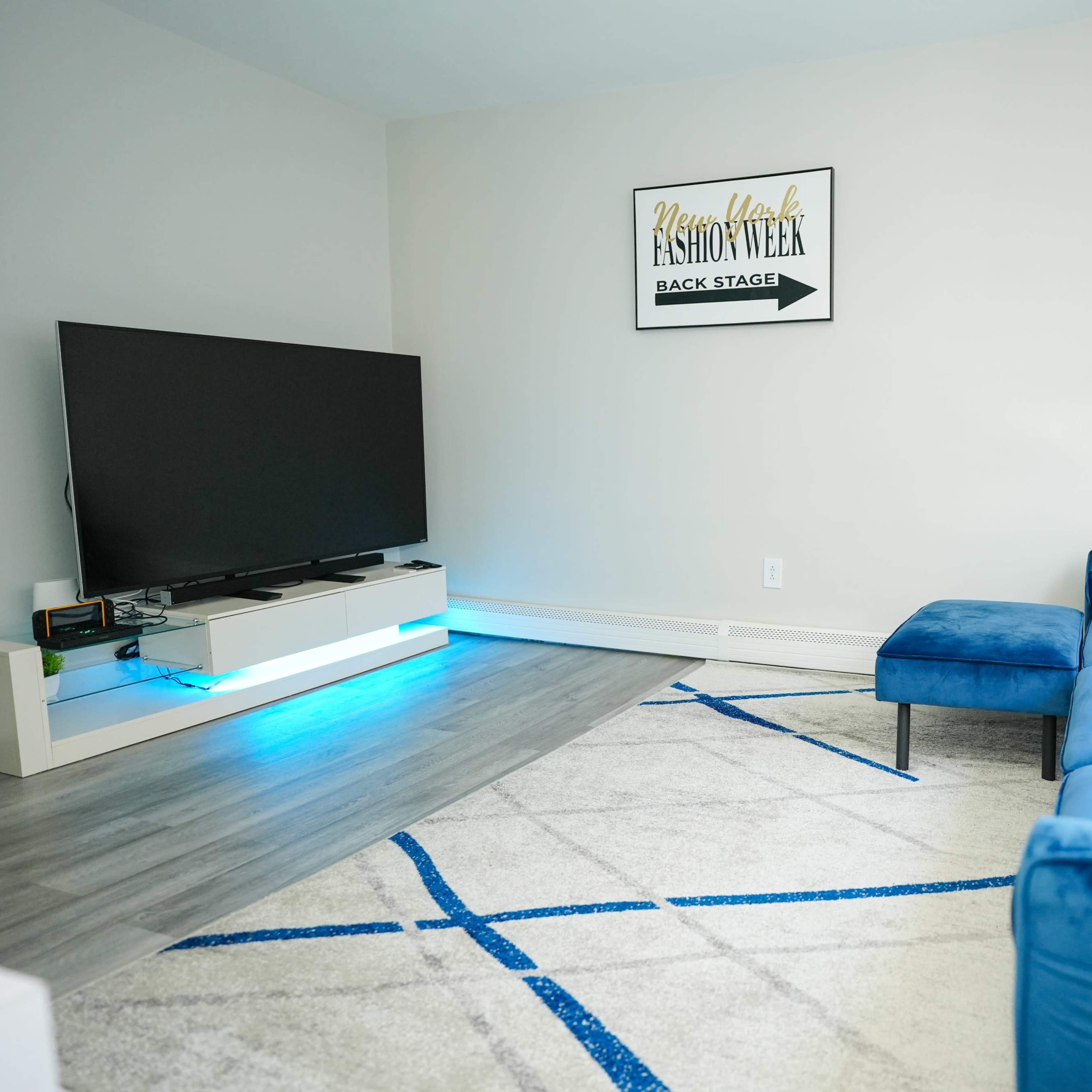 A modern living room with a blue sectional sofa, a large television on a white stand, and a decorative plant beside a light-colored rug.