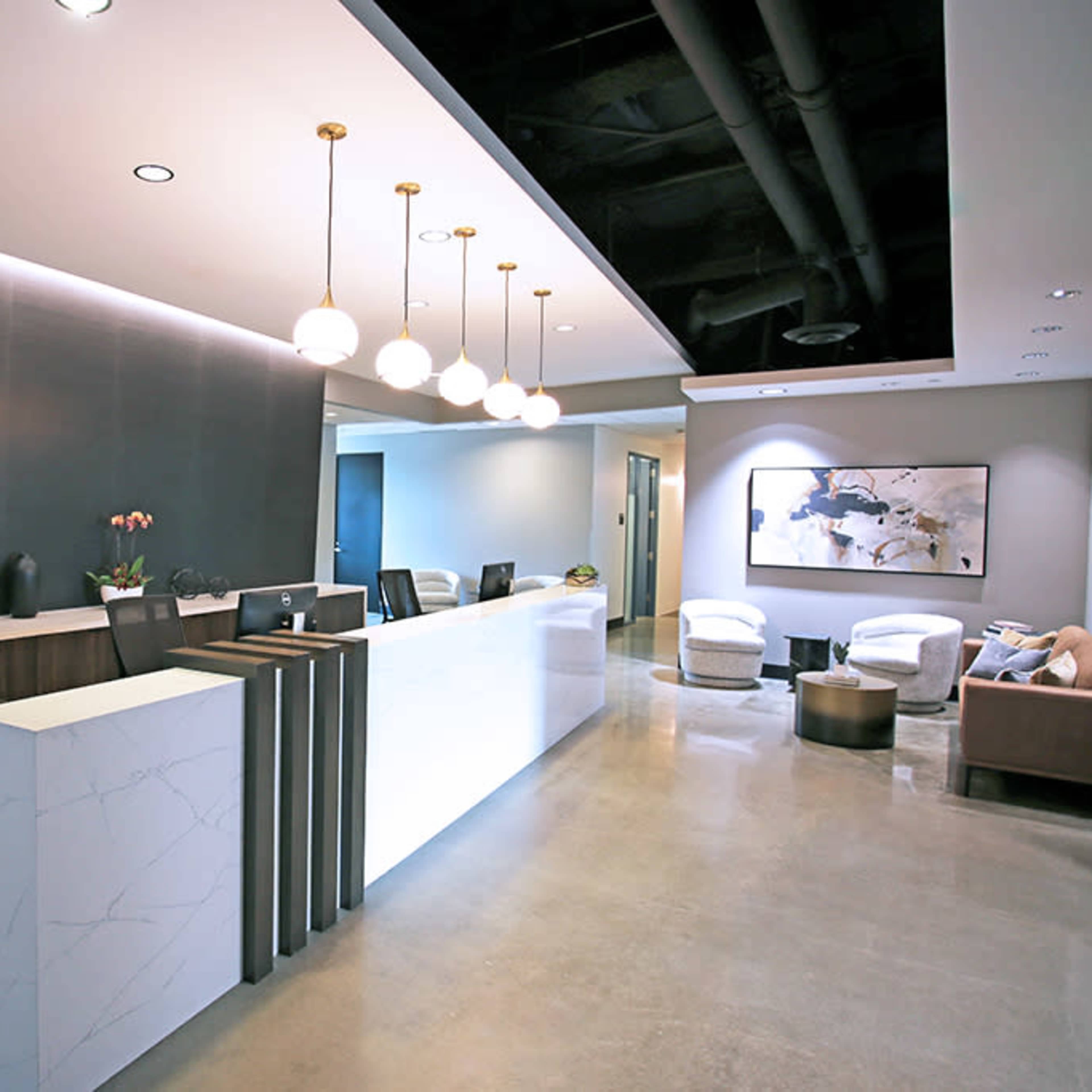 A modern reception area with a sleek front desk, decorative lighting, and seating arrangements.