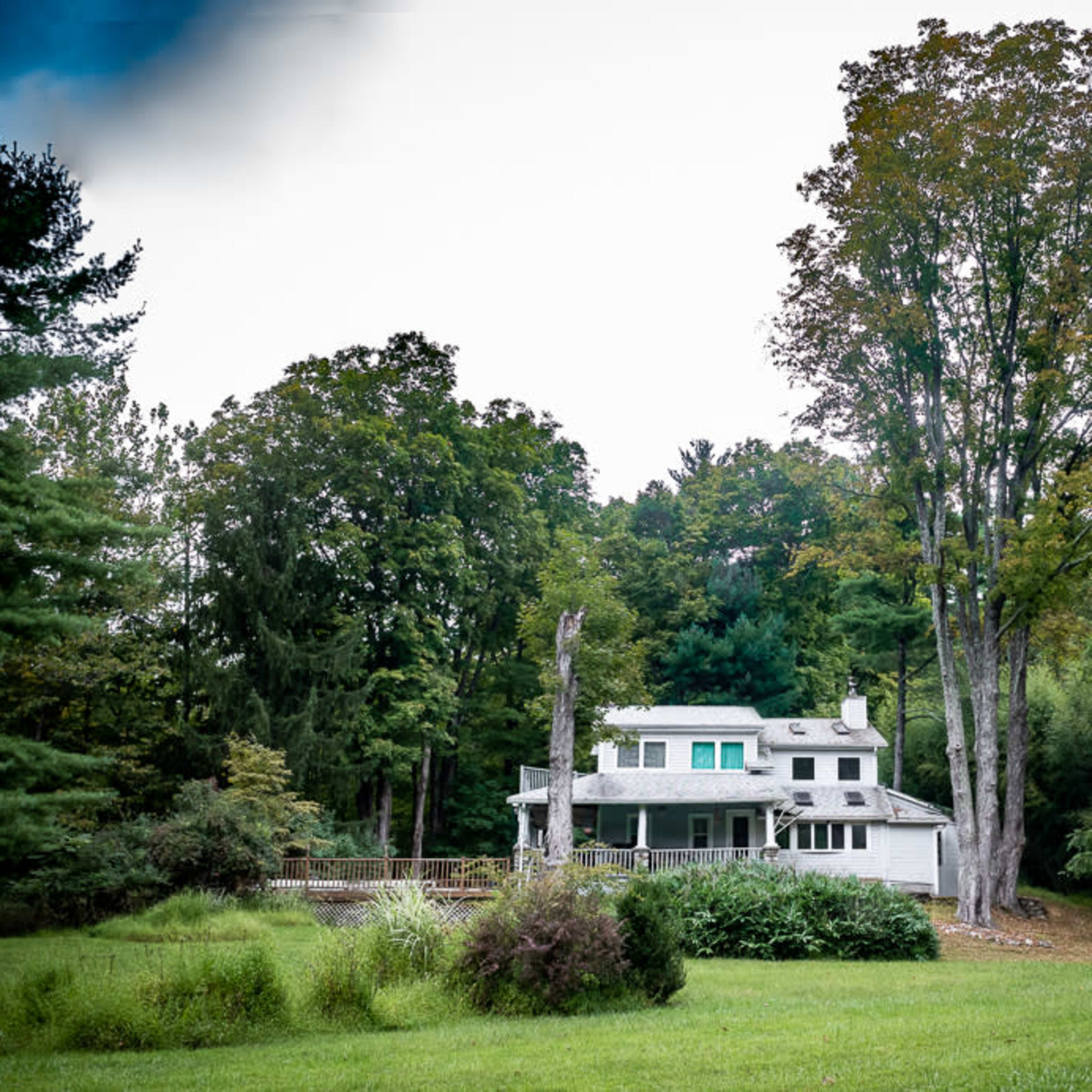 A large white house surrounded by trees and a grassy area is set against a hillside.