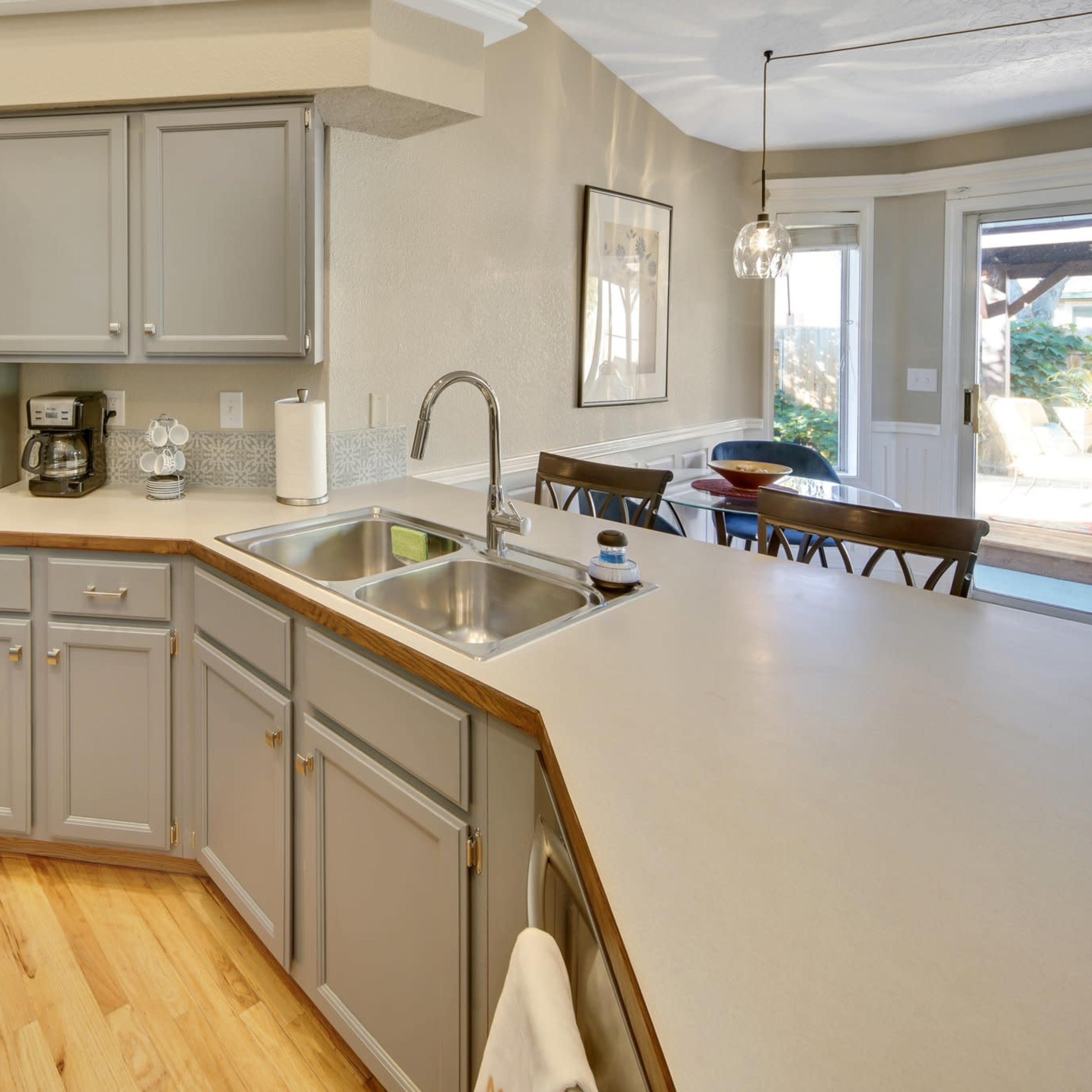A modern kitchen with stainless steel appliances, gray cabinetry, and a wooden countertop.
