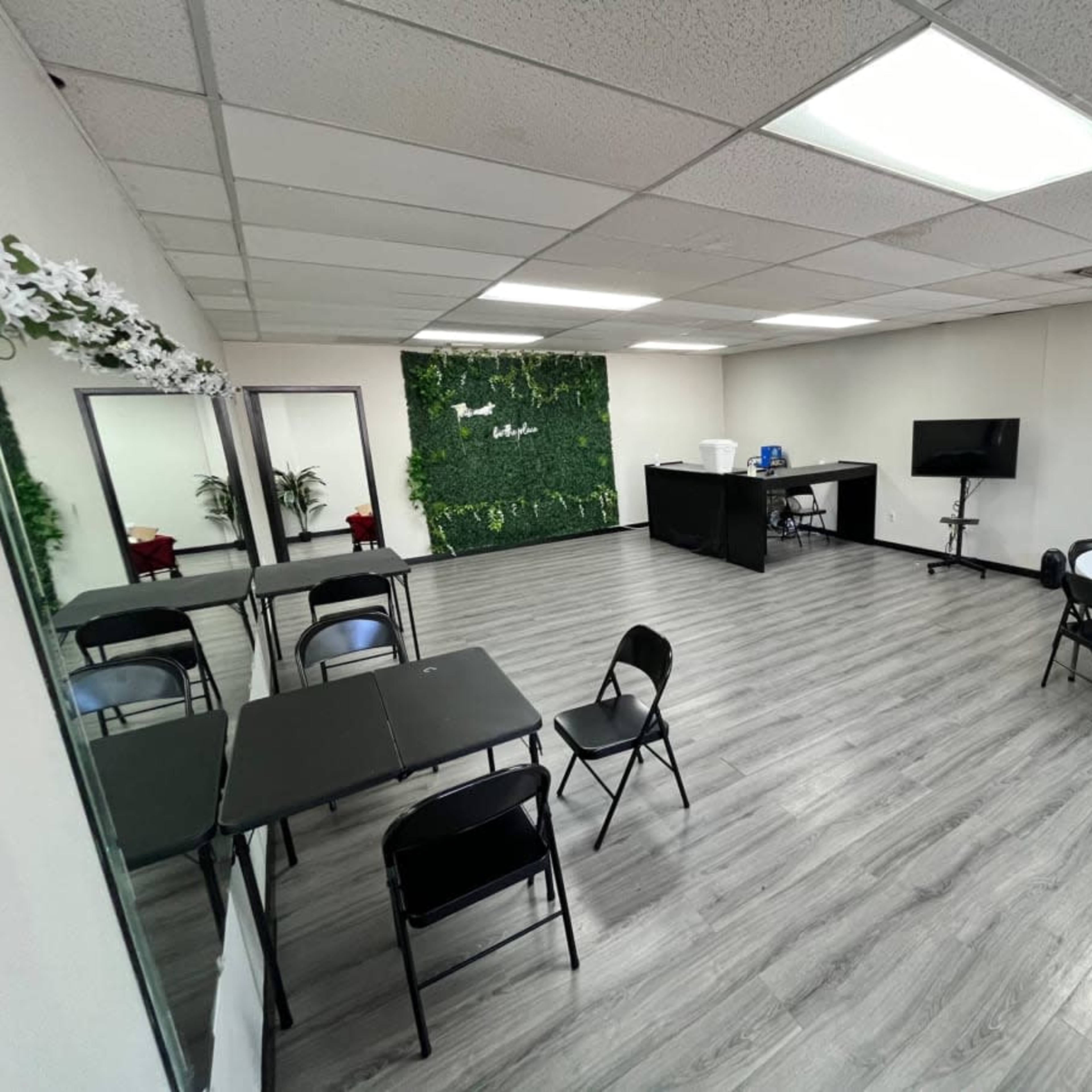 A spacious meeting room with tables and chairs arranged, a green plant wall, and a television setup.