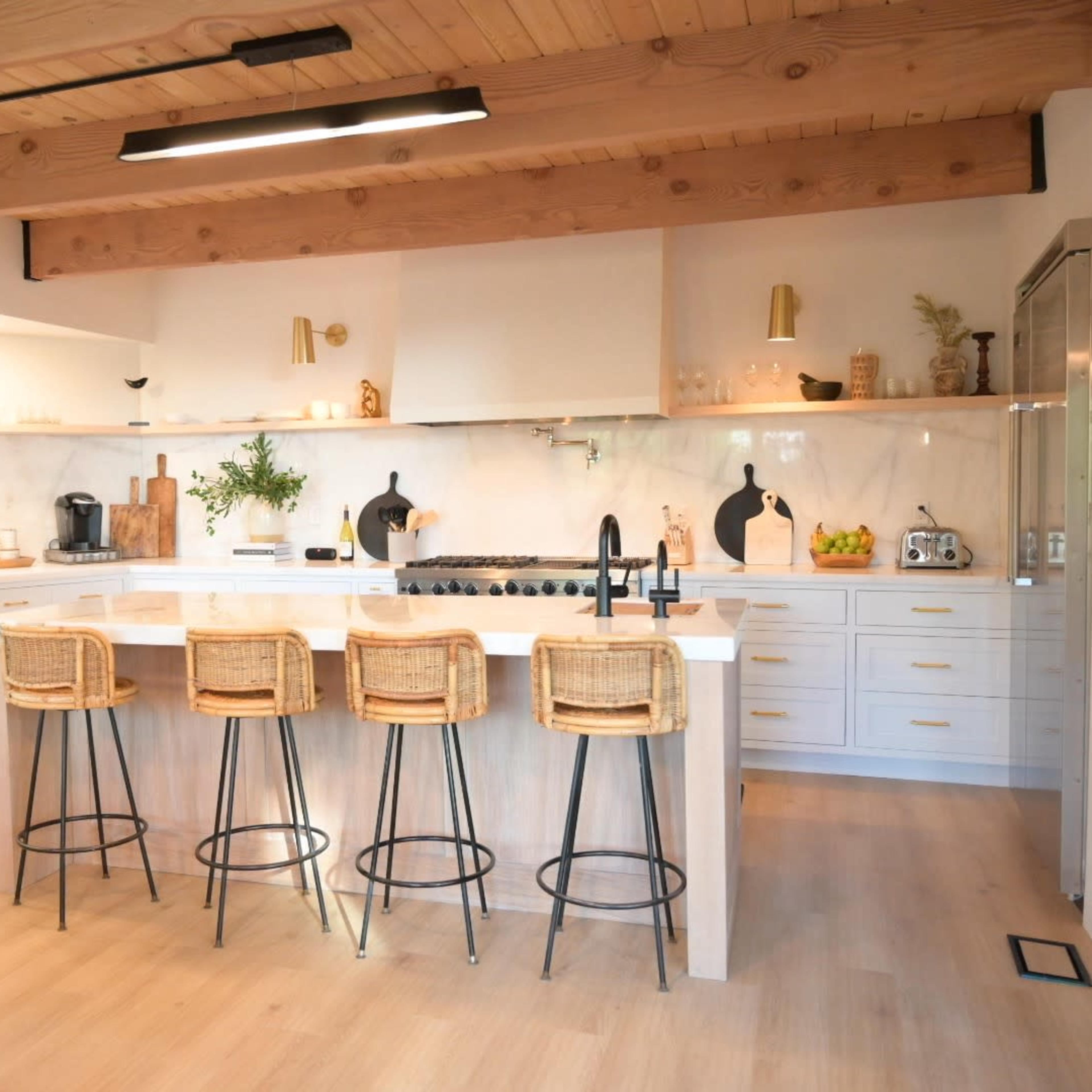 A modern kitchen with a large island, four bar stools, and a combination of white cabinetry and wooden accents.