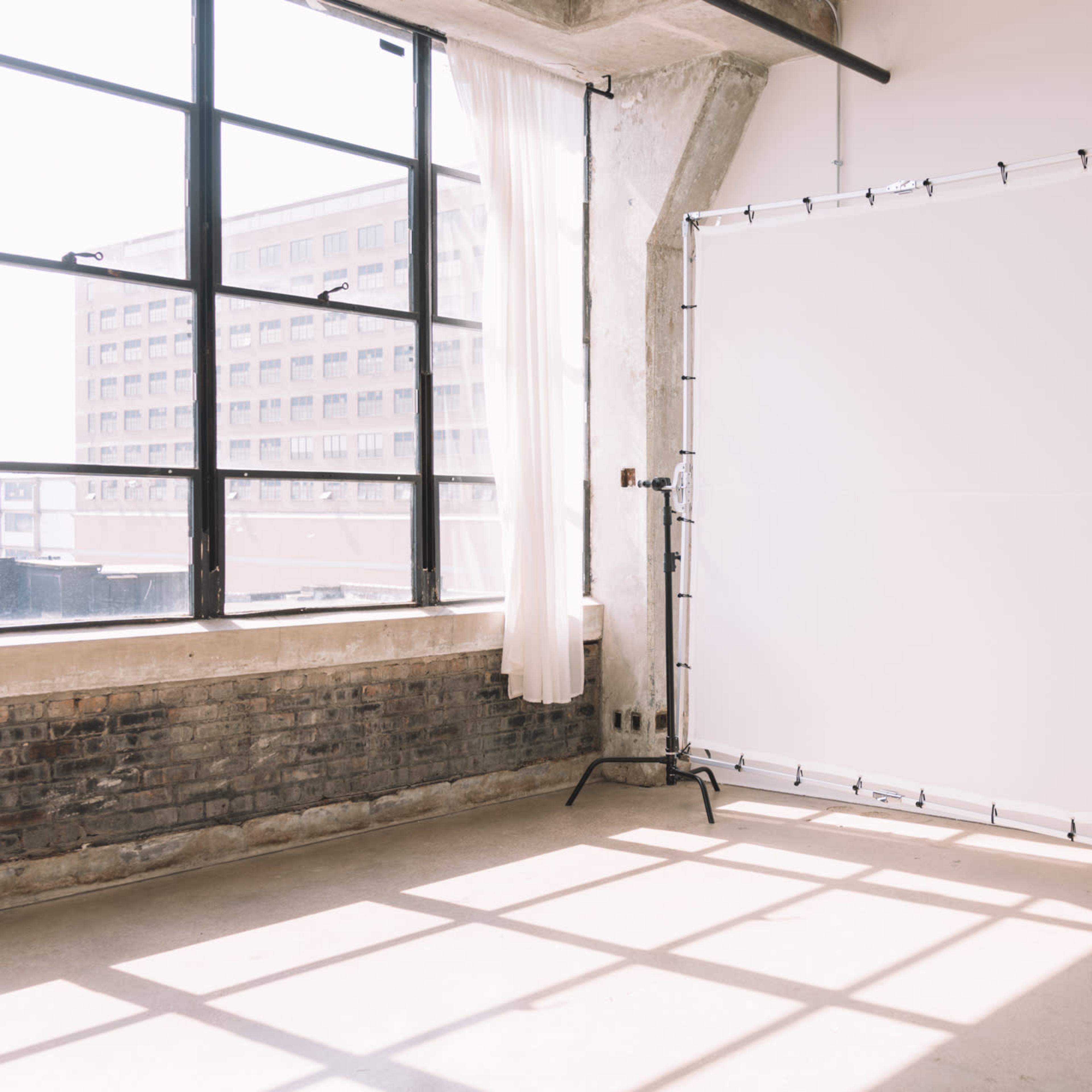 A white backdrop stands on a black frame in a well-lit industrial space with large windows.