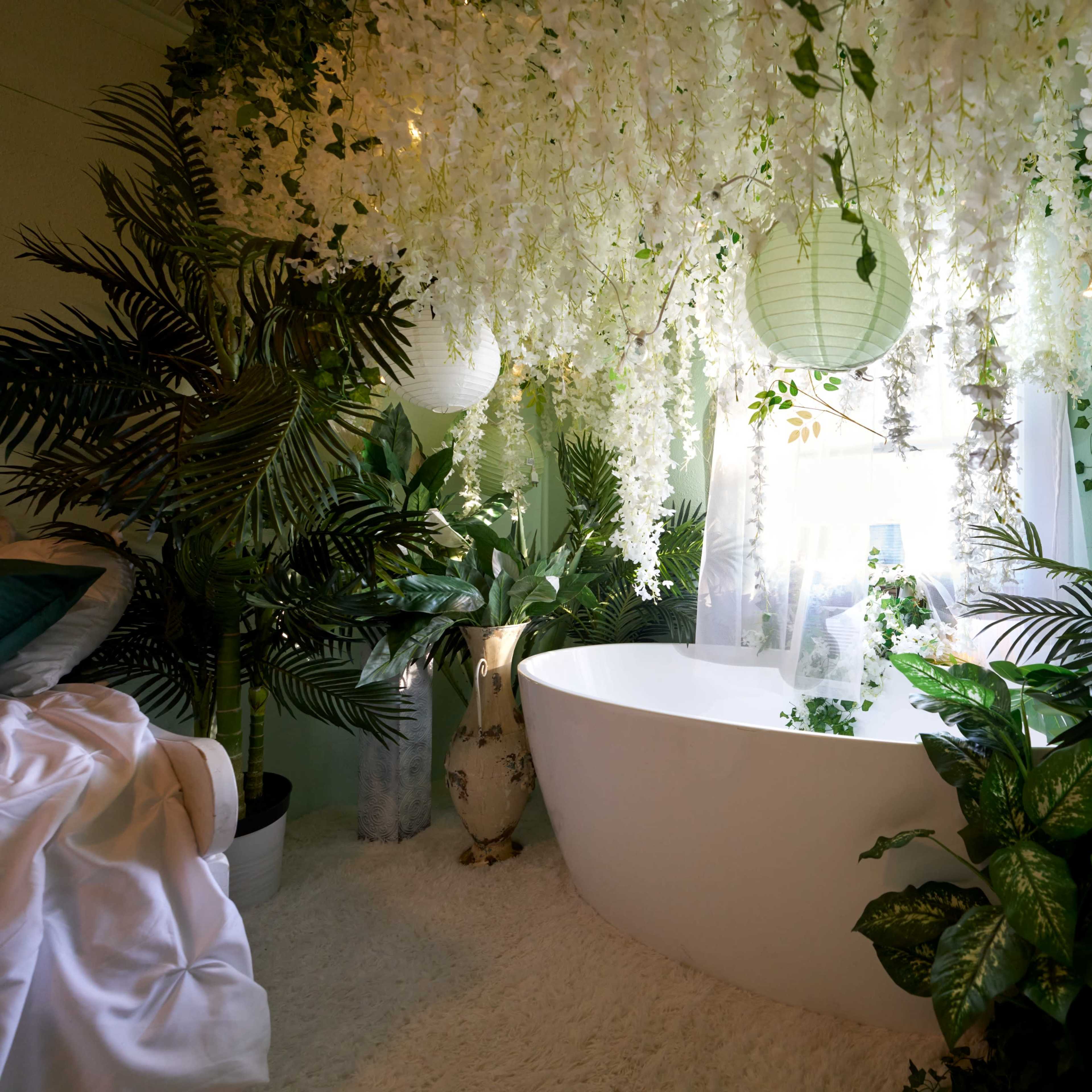 A modern bathroom with a freestanding white bathtub surrounded by lush greenery and decorative hanging plants.