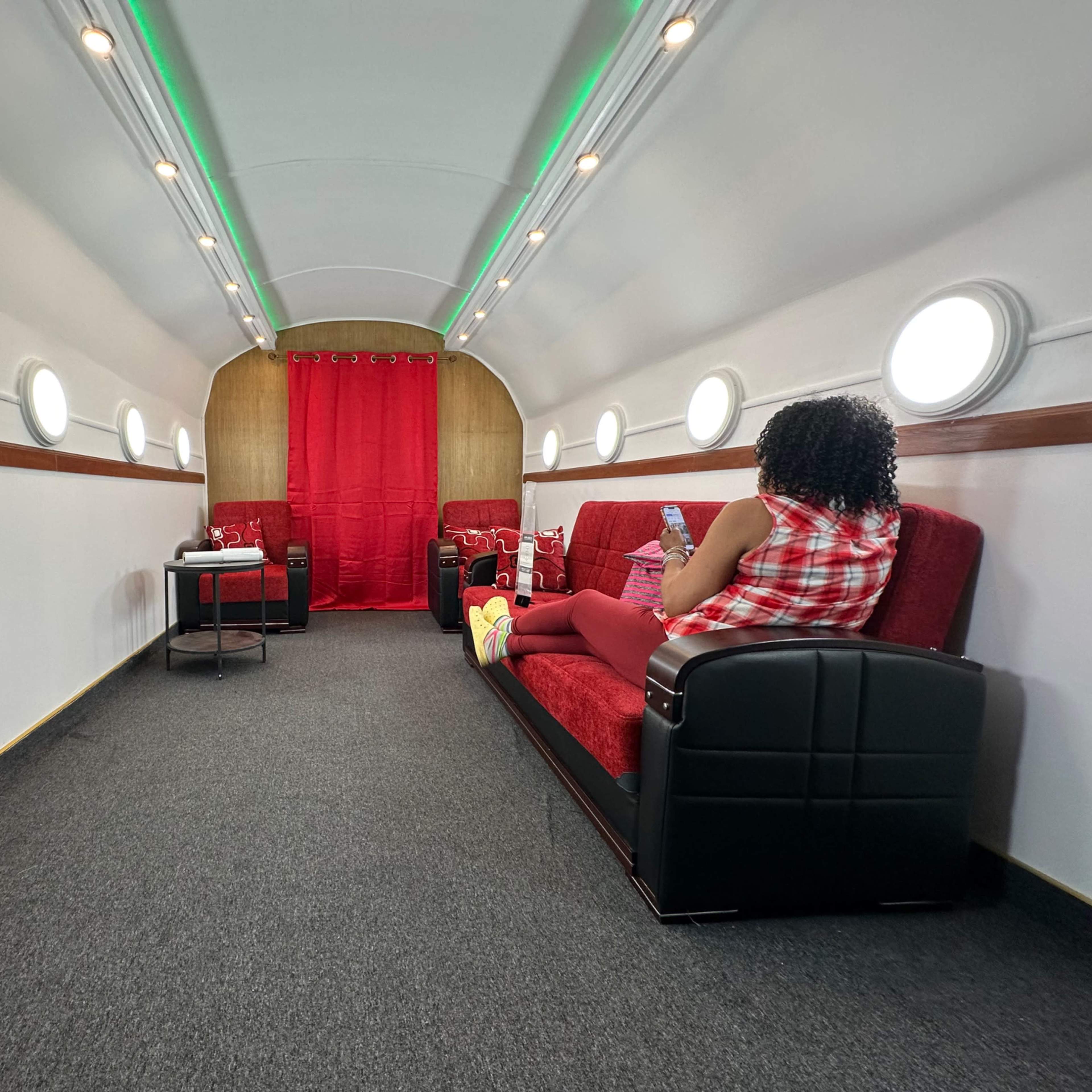 The interior of a trailer is lined with red seating and features circular windows along the walls, creating a cozy atmosphere.