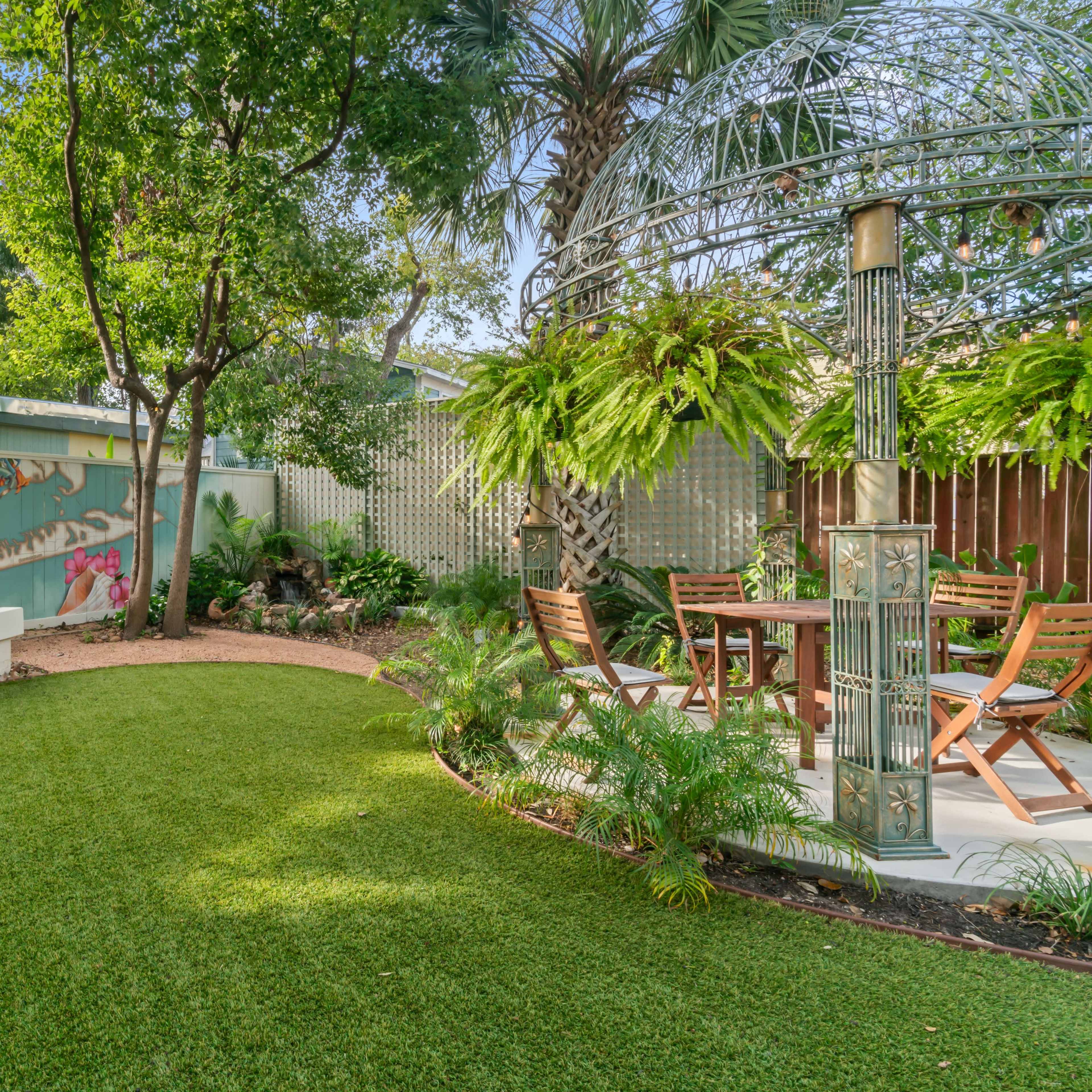 A landscaped garden with artificial grass, a white bench, and a dining area surrounded by greenery and a mural depicting wildlife.