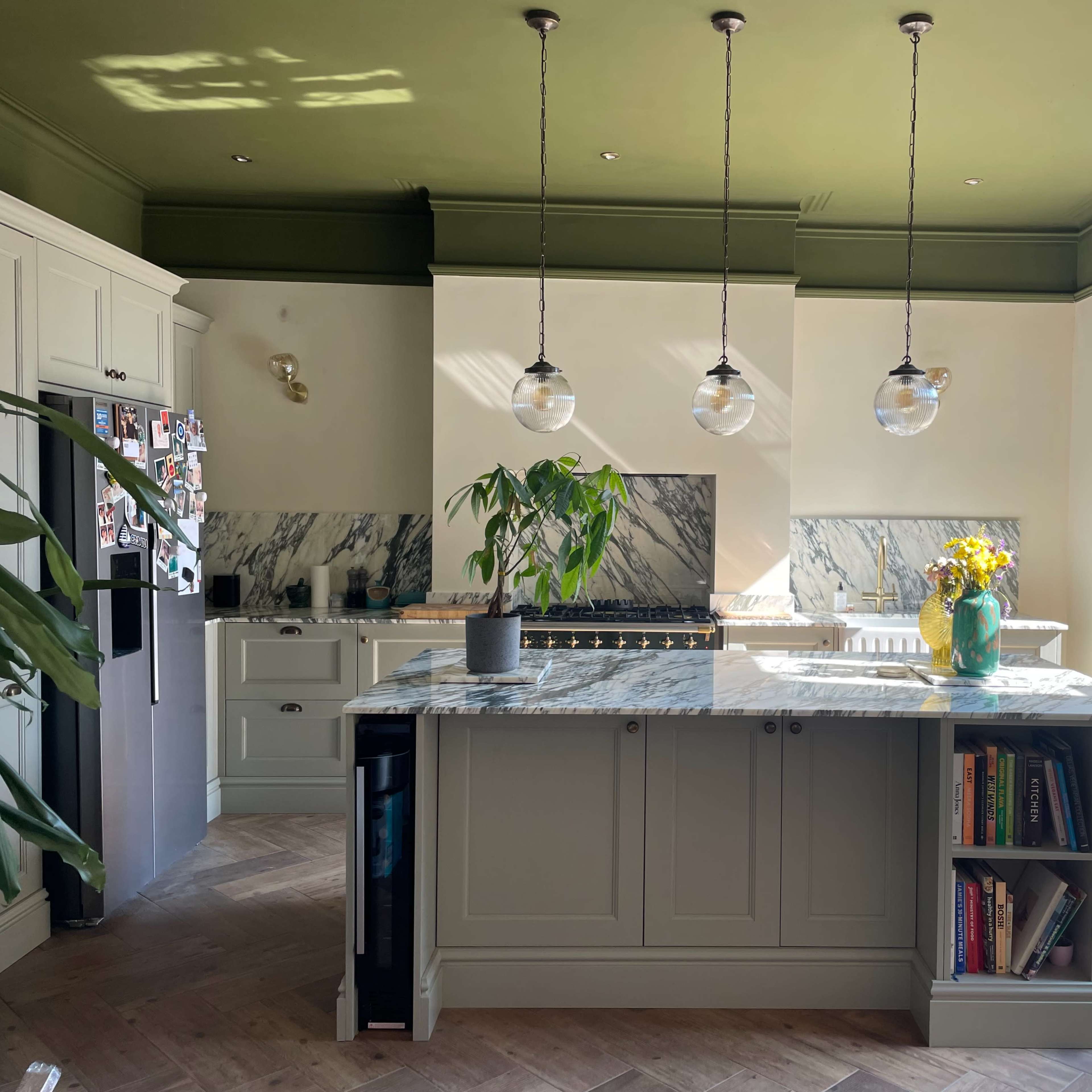 The kitchen features a central island with a marble countertop, three pendant lights above, and large windows providing natural light.