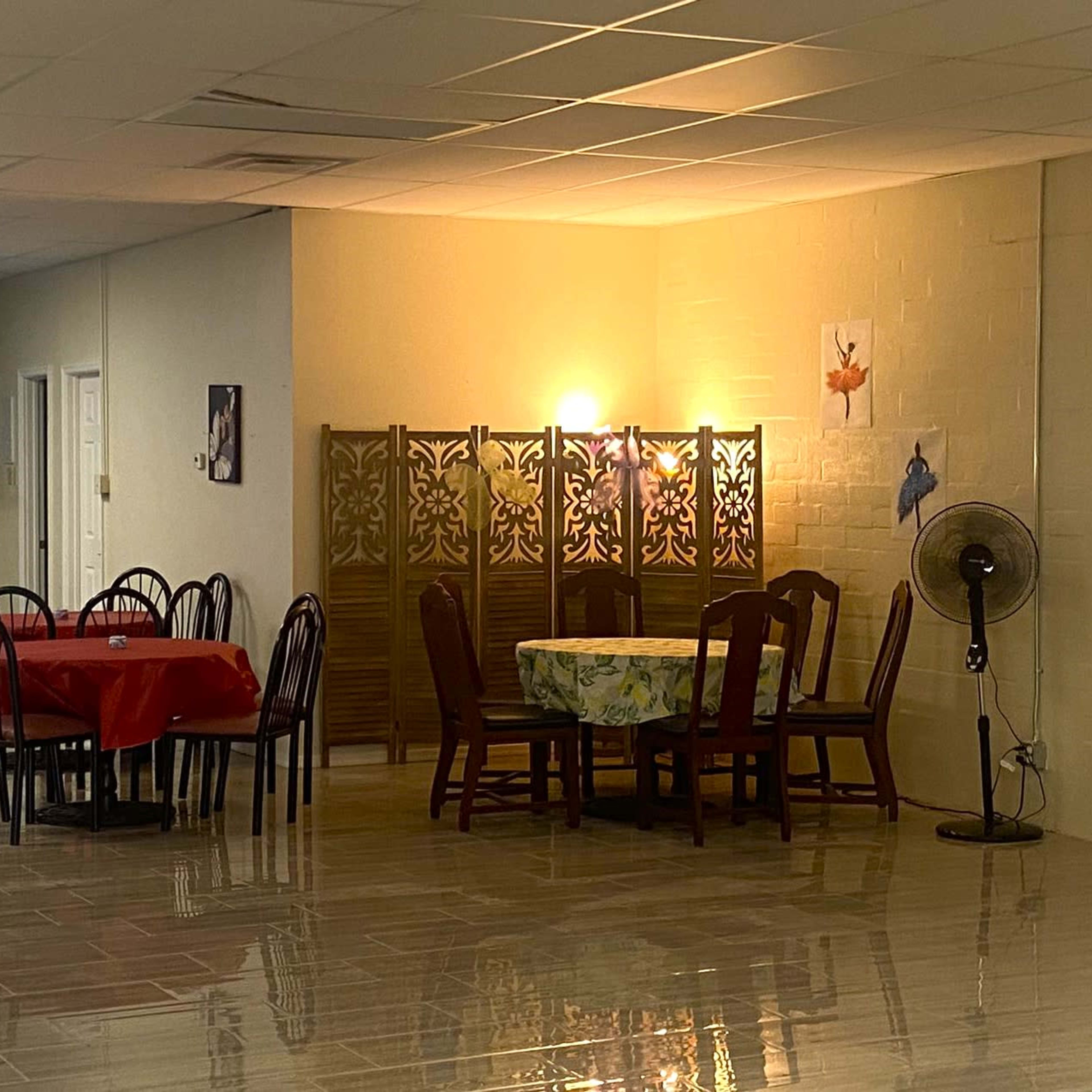A dining area with tables and chairs, a decorative folding screen, and a fan in a well-lit room.