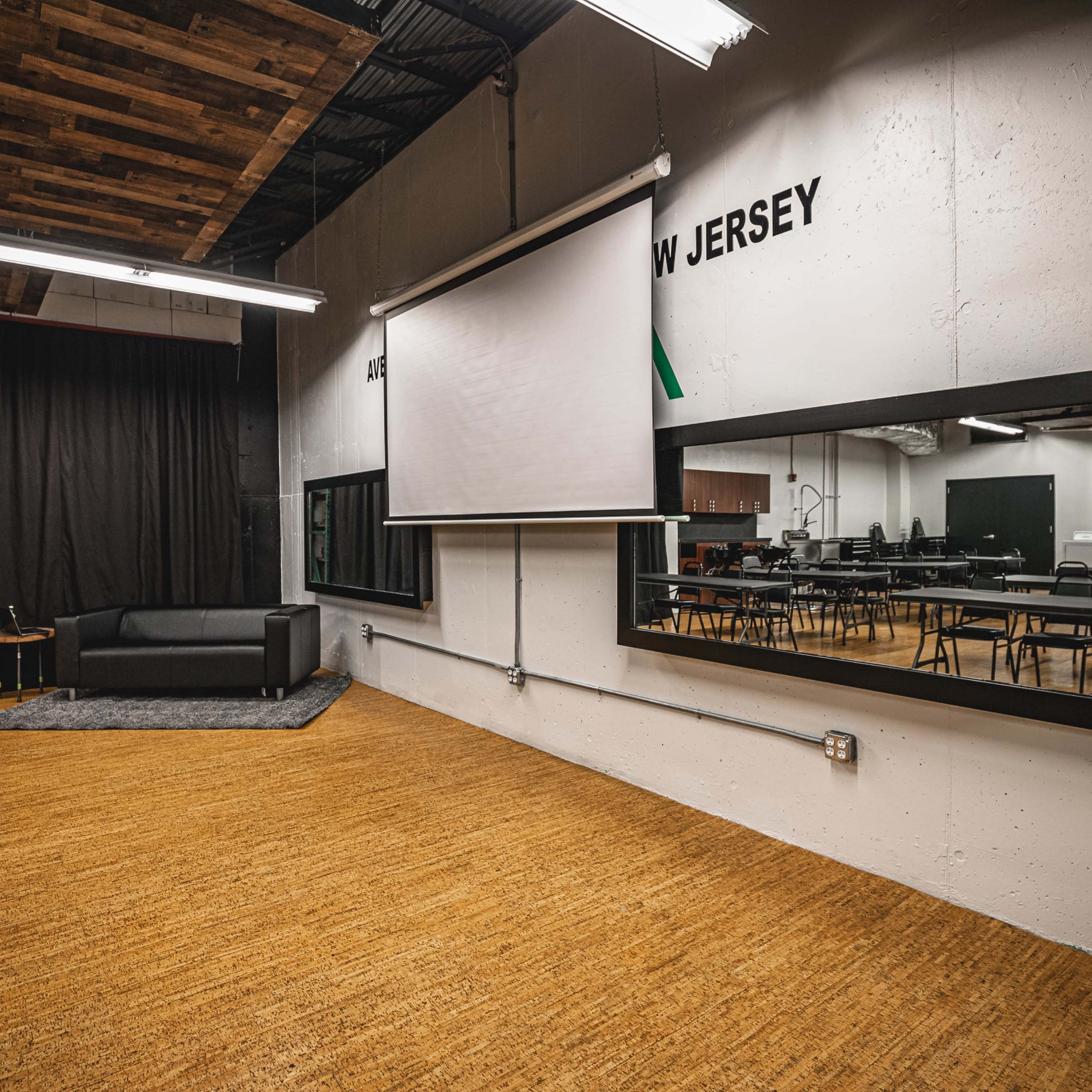 A spacious classroom or workshop area with a black sofa, a large mirror, and multiple tables arranged for use.