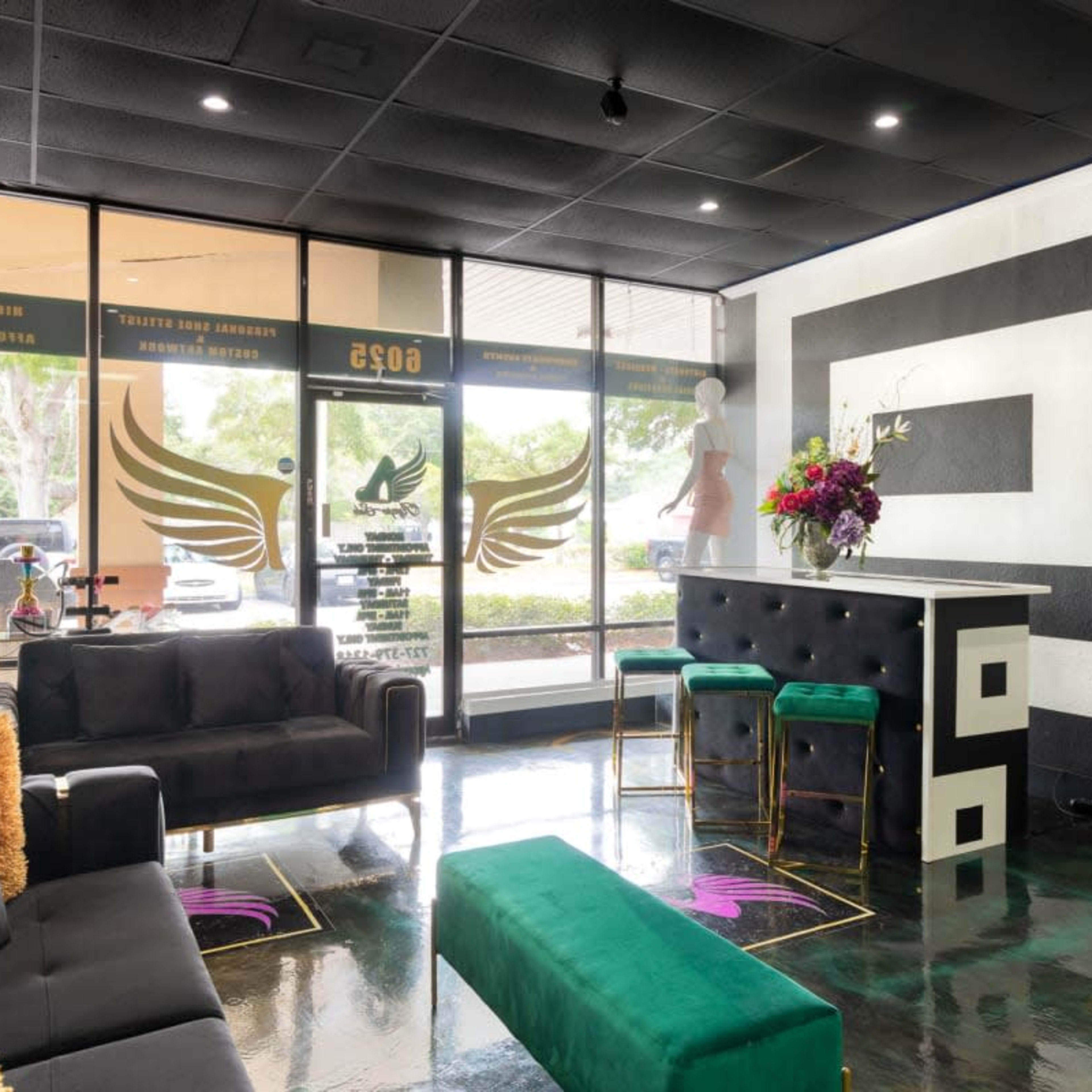 A modern interior of a lounge area with black sofas, a green bench, and a bar-style table, featuring large windows that provide a view of the outside.