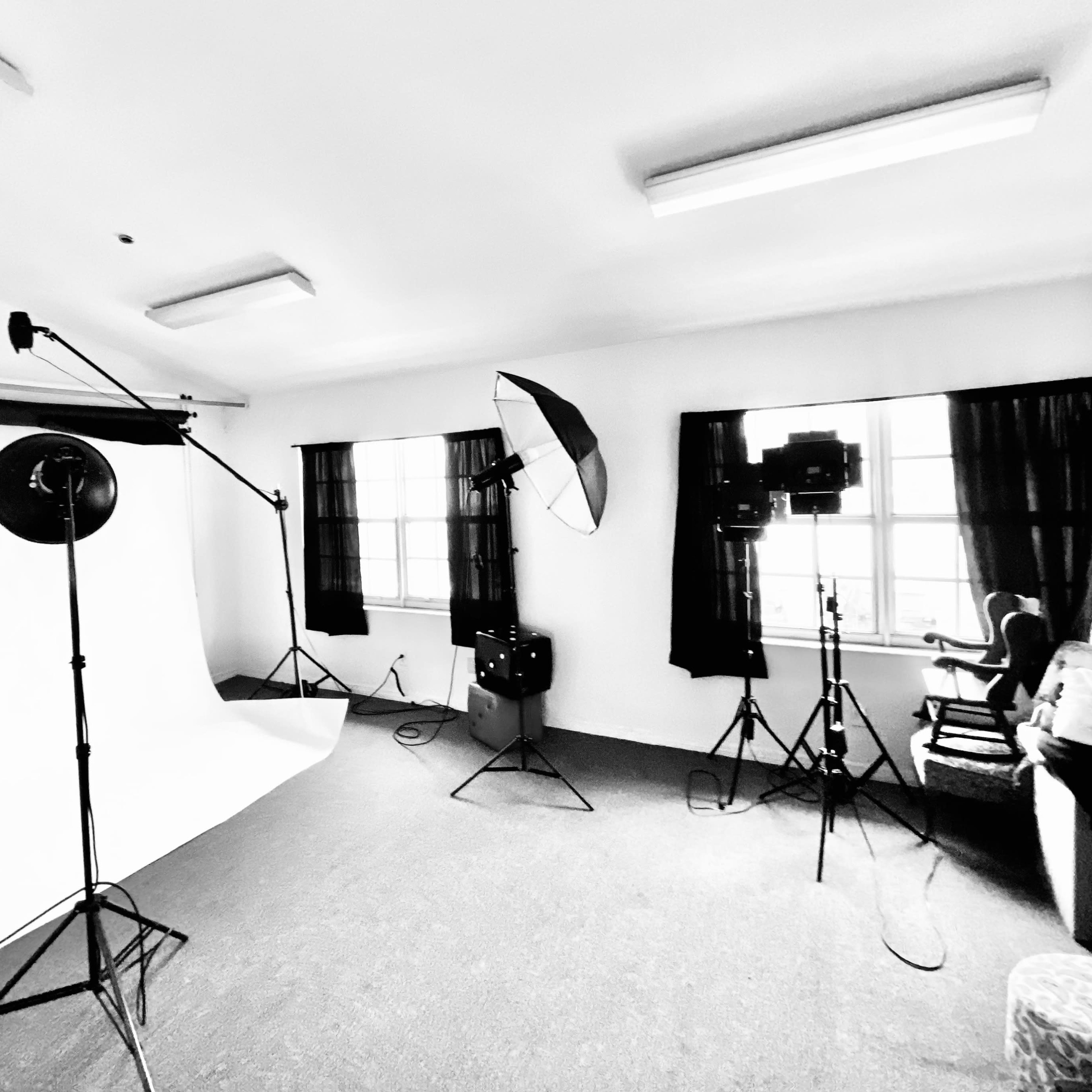 A photography studio with a white backdrop, lighting equipment, and a chair positioned in front of the window.